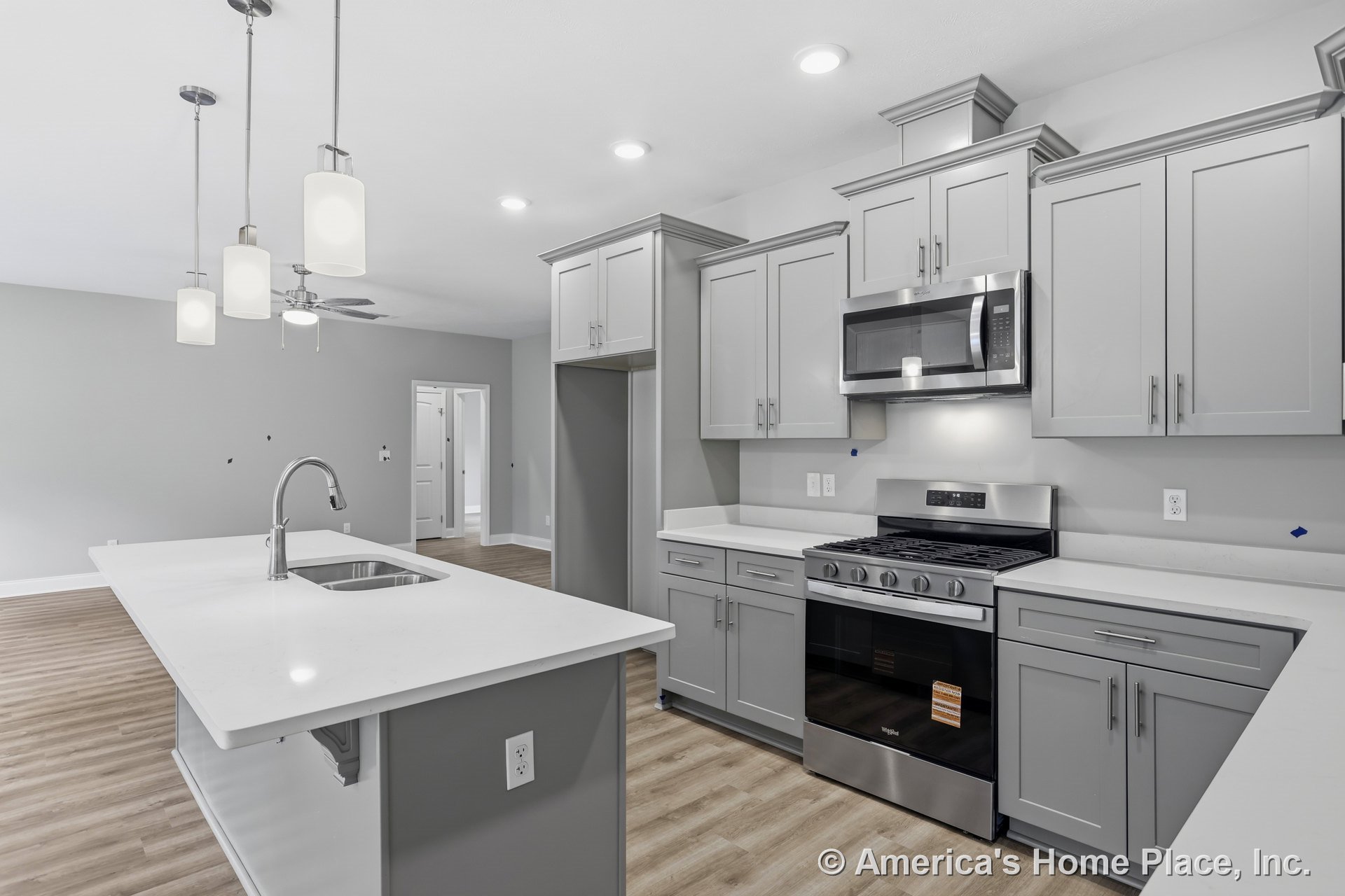 Gray shaker cabinets with white quartz countertops, stainless steel range and microwave, pendant lights above island sink, recessed ceiling lighting, wood-look vinyl flooring