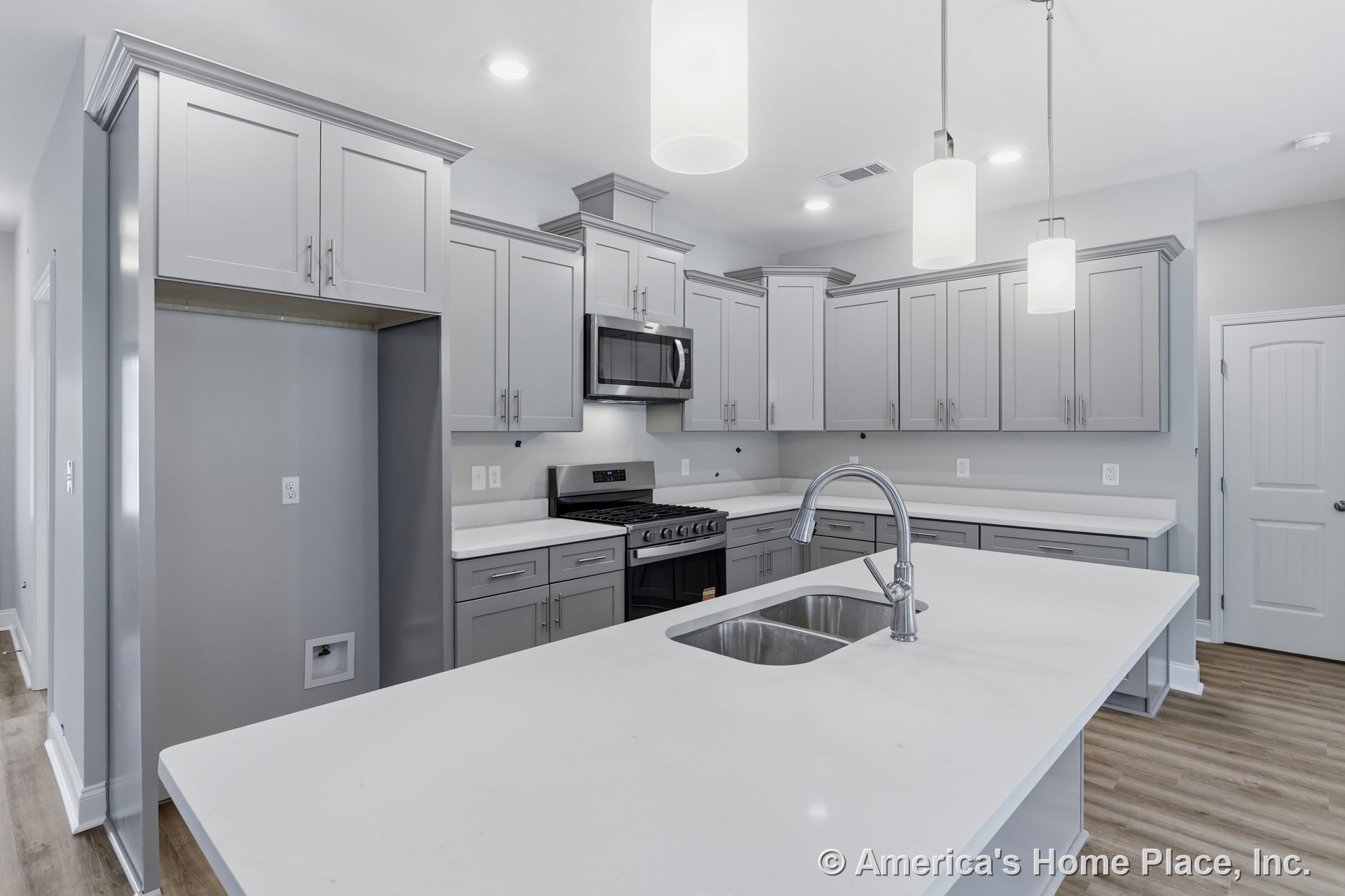 Gray shaker cabinets and quartz countertops with a large kitchen island featuring an undermount stainless sink, pendant and recessed lighting, stainless appliances including