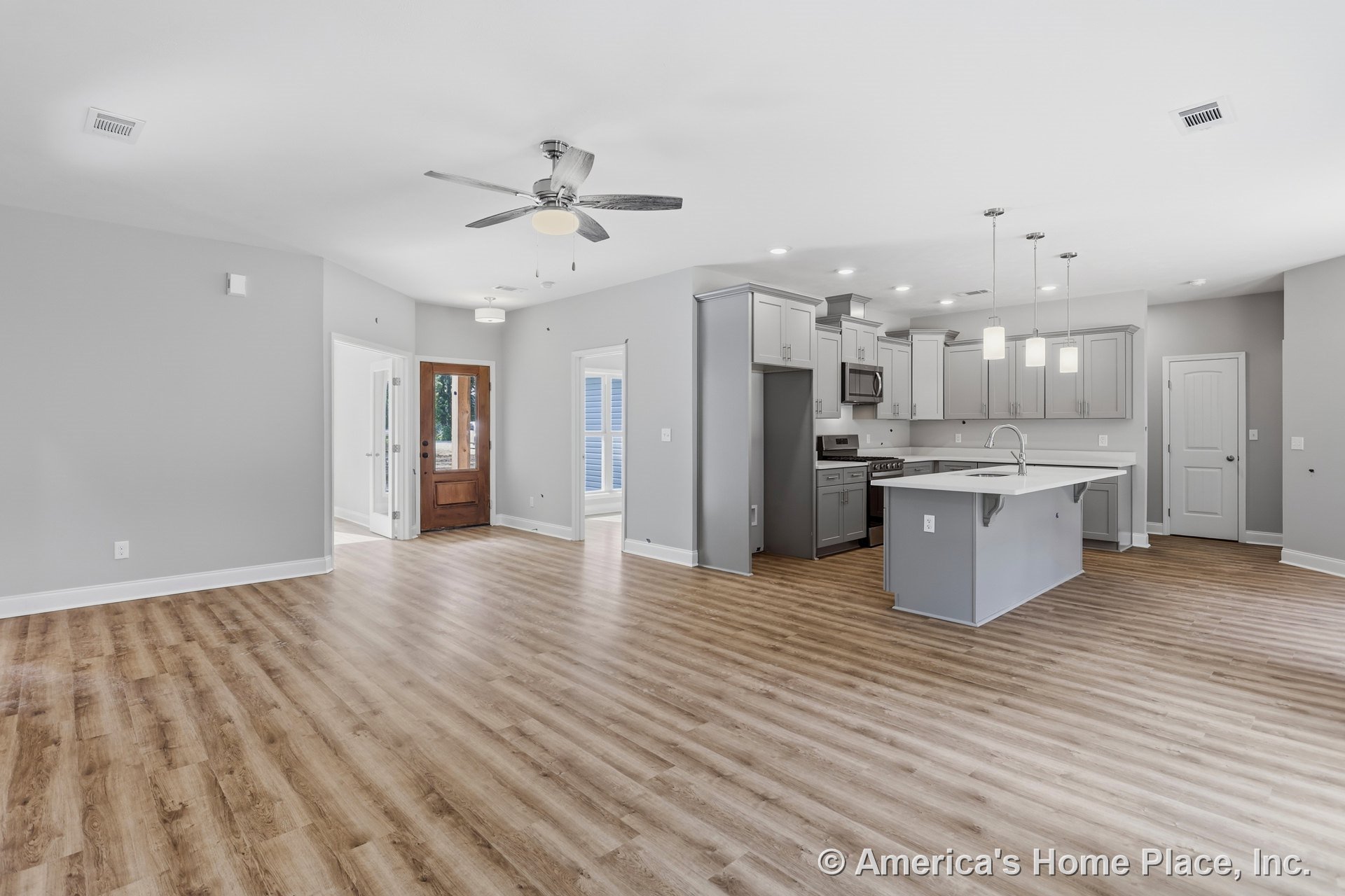 Open-concept kitchen and living area with gray cabinetry, large central island featuring sink and pendant lights, wood-look vinyl plank flooring, recessed ceiling lighting