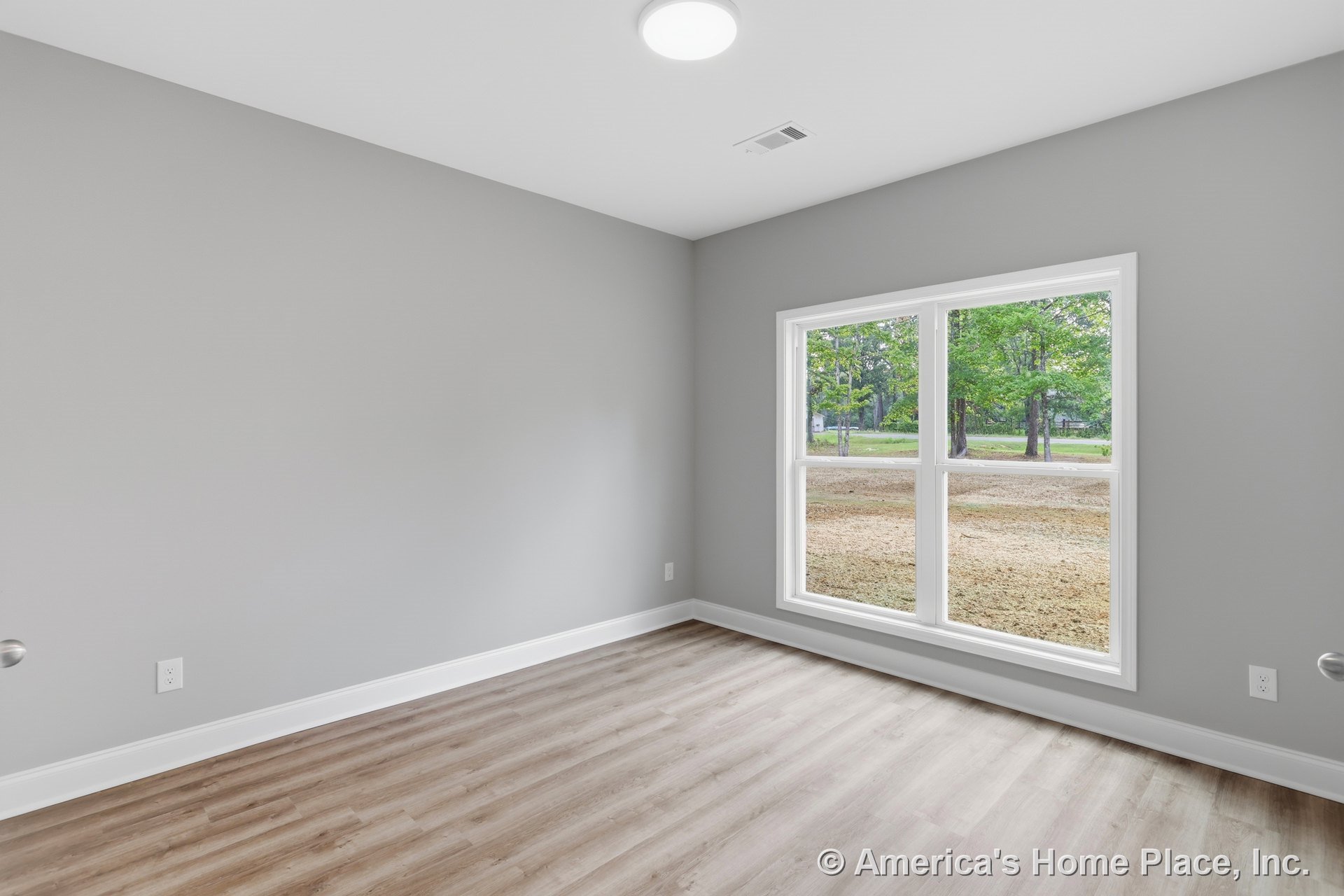 Bedroom with light wood plank flooring, large double window, gray painted walls, white baseboard trim, flush ceiling light fixture, and rectangular layout.