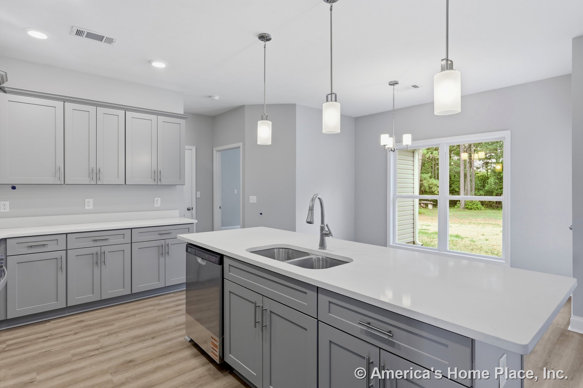 Gray shaker cabinets with quartz countertops, double-basin undermount sink, pendant lights above the island, large window, light wood flooring, built-in dishwasher, and recessed