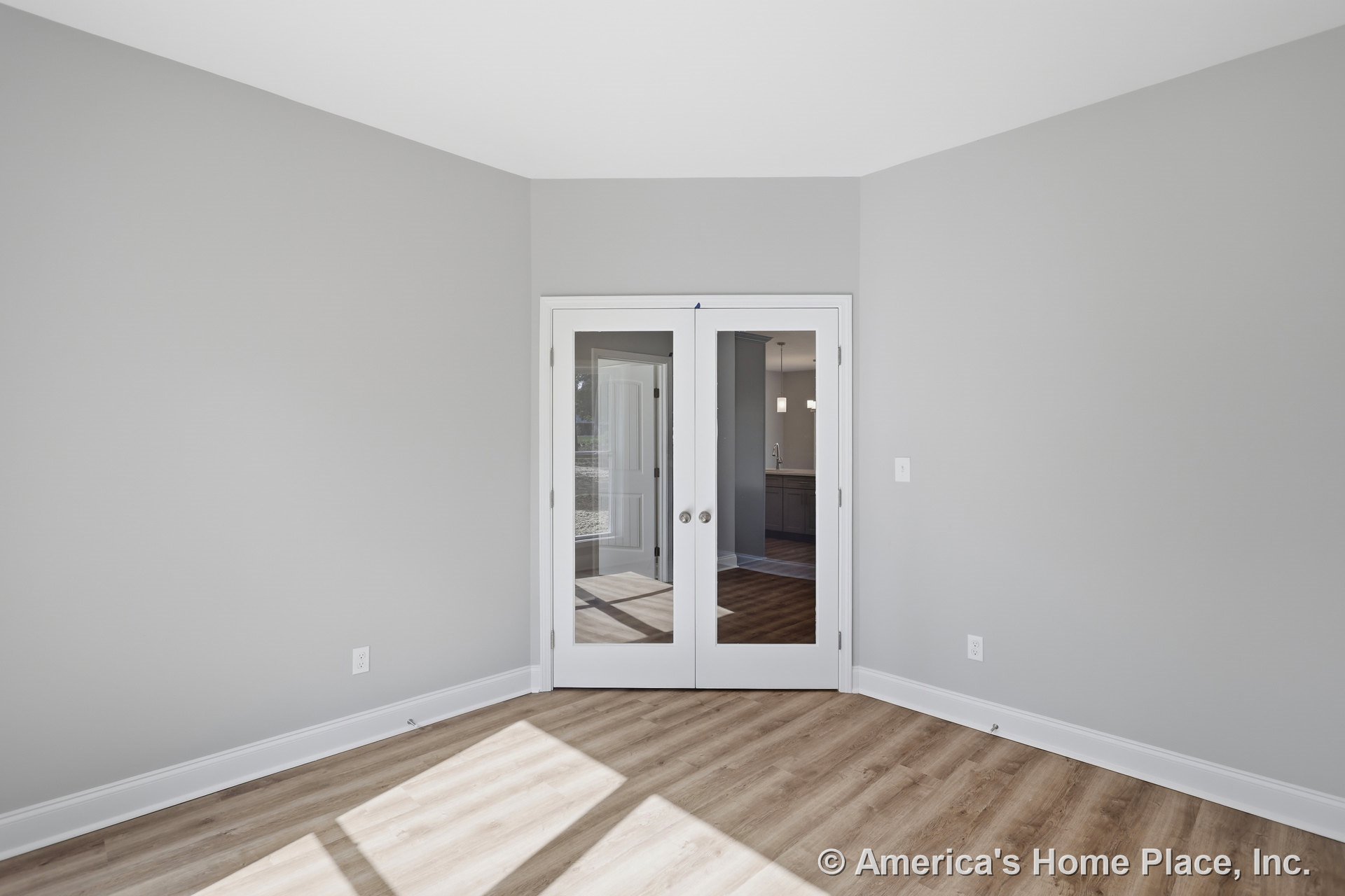 Double glass French doors open to a room with light wood plank flooring, gray painted walls, white baseboard trim, smooth ceiling, and recessed electrical outlets.