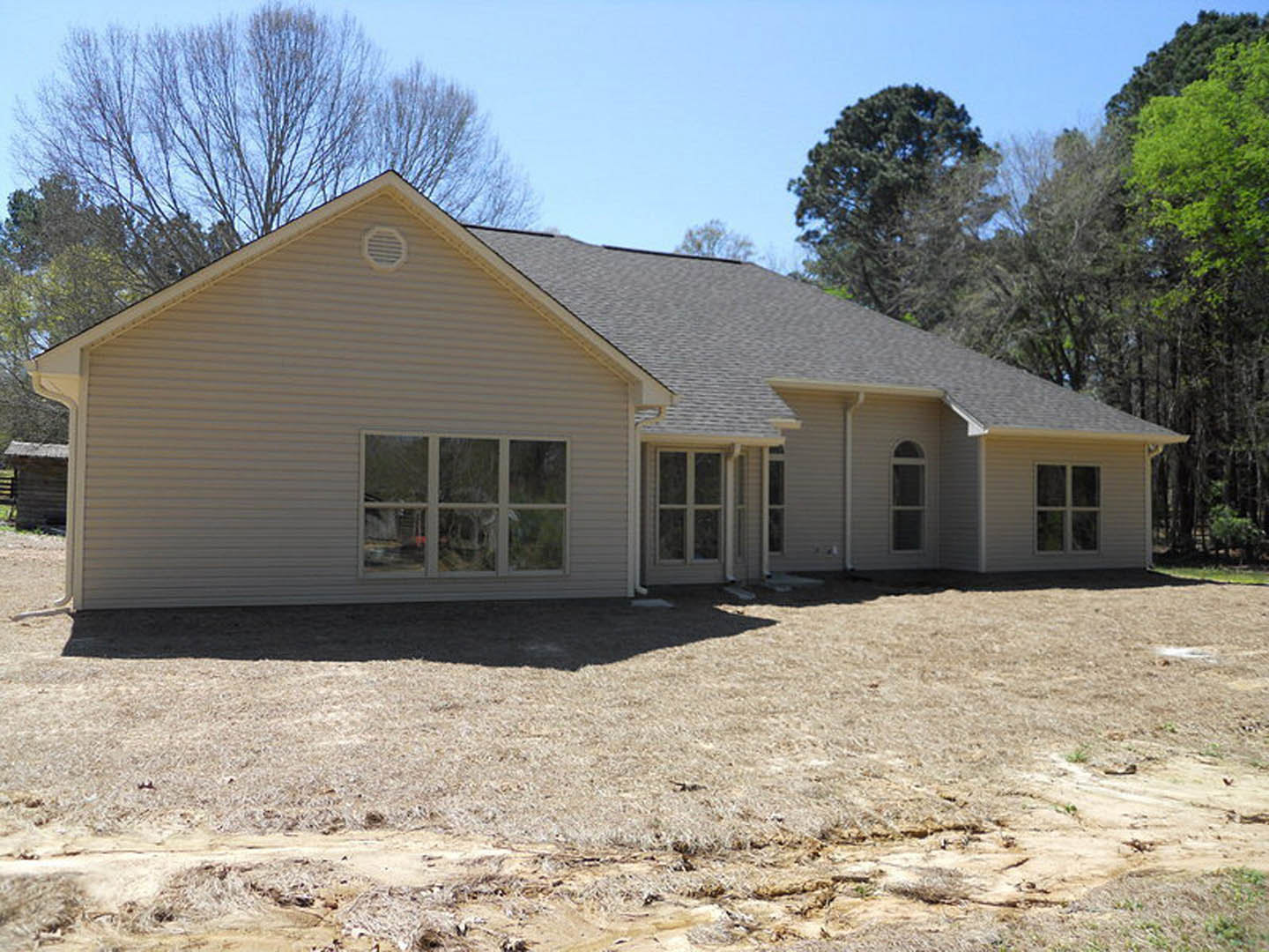 Two-story home with large multi-pane white-framed windows, exterior vent, patchy grass, and exposed dirt yard under a clear sky.