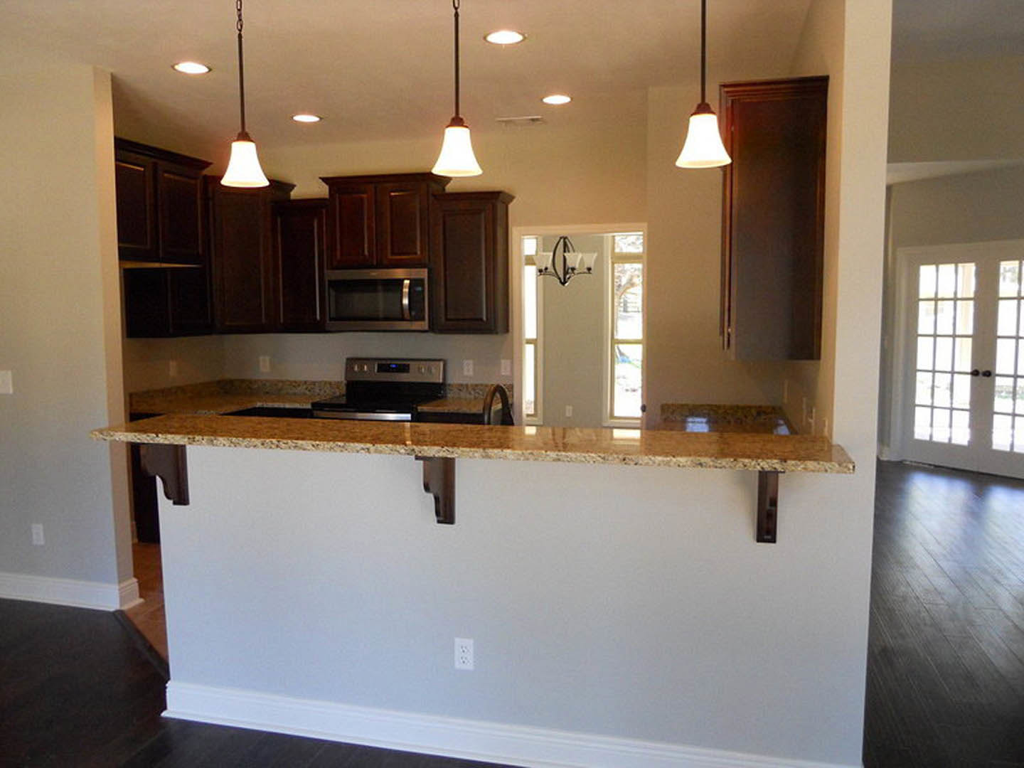Granite countertop kitchen with wood cabinetry, stainless steel microwave and stove, tile backsplash, and hardwood flooring