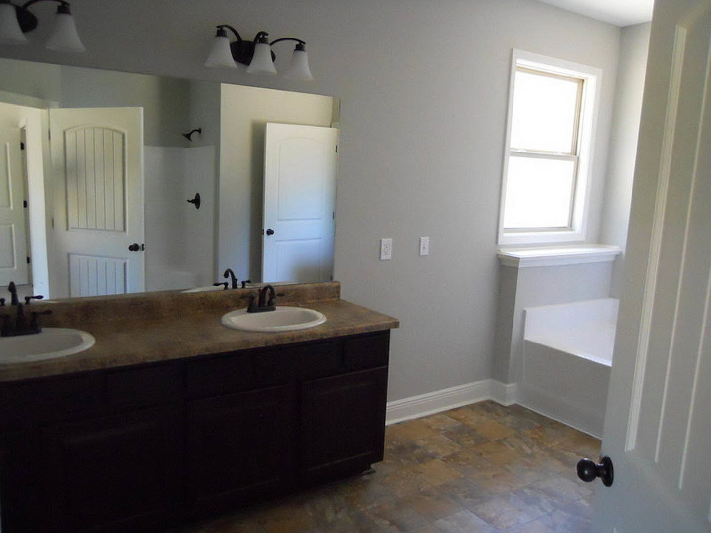 Modern bathroom featuring a freestanding bathtub, double sinks with chrome faucets, white tile flooring, and light fixtures mounted on a white wall.