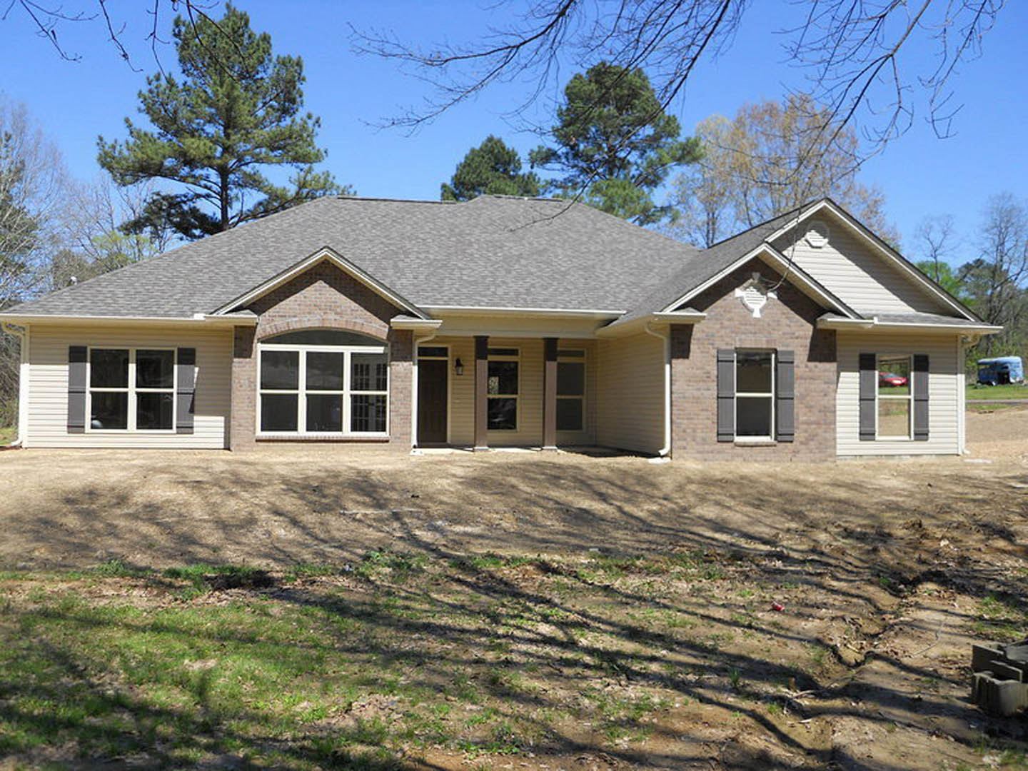 Two-story house with white siding, covered front porch, white-framed windows, and a grassy yard bordered by tall trees in the background