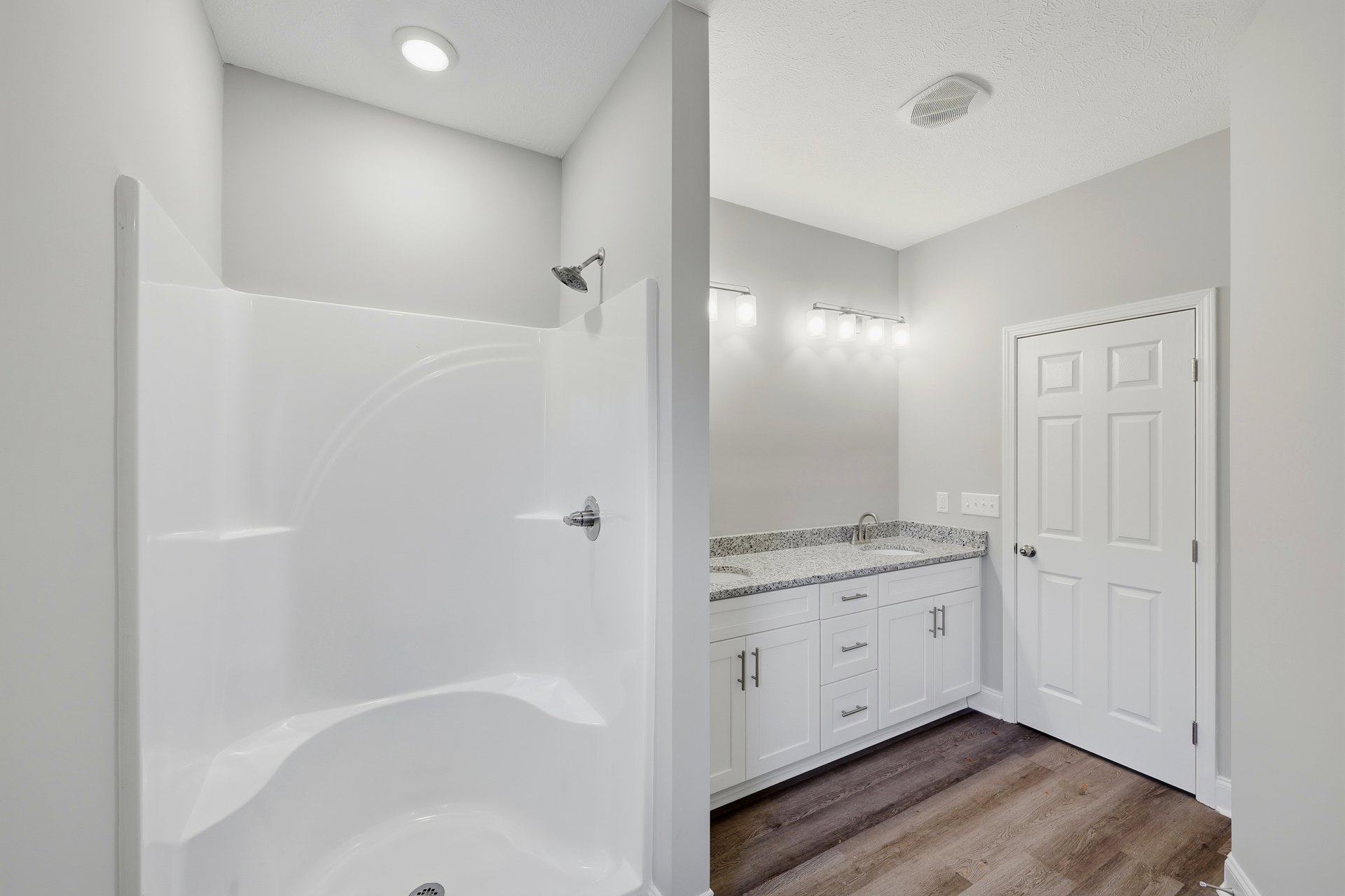 Bathroom featuring white tile shower with silver showerhead, white bathtub with chrome faucet, white door with silver knobs, and white sink with metal faucet.