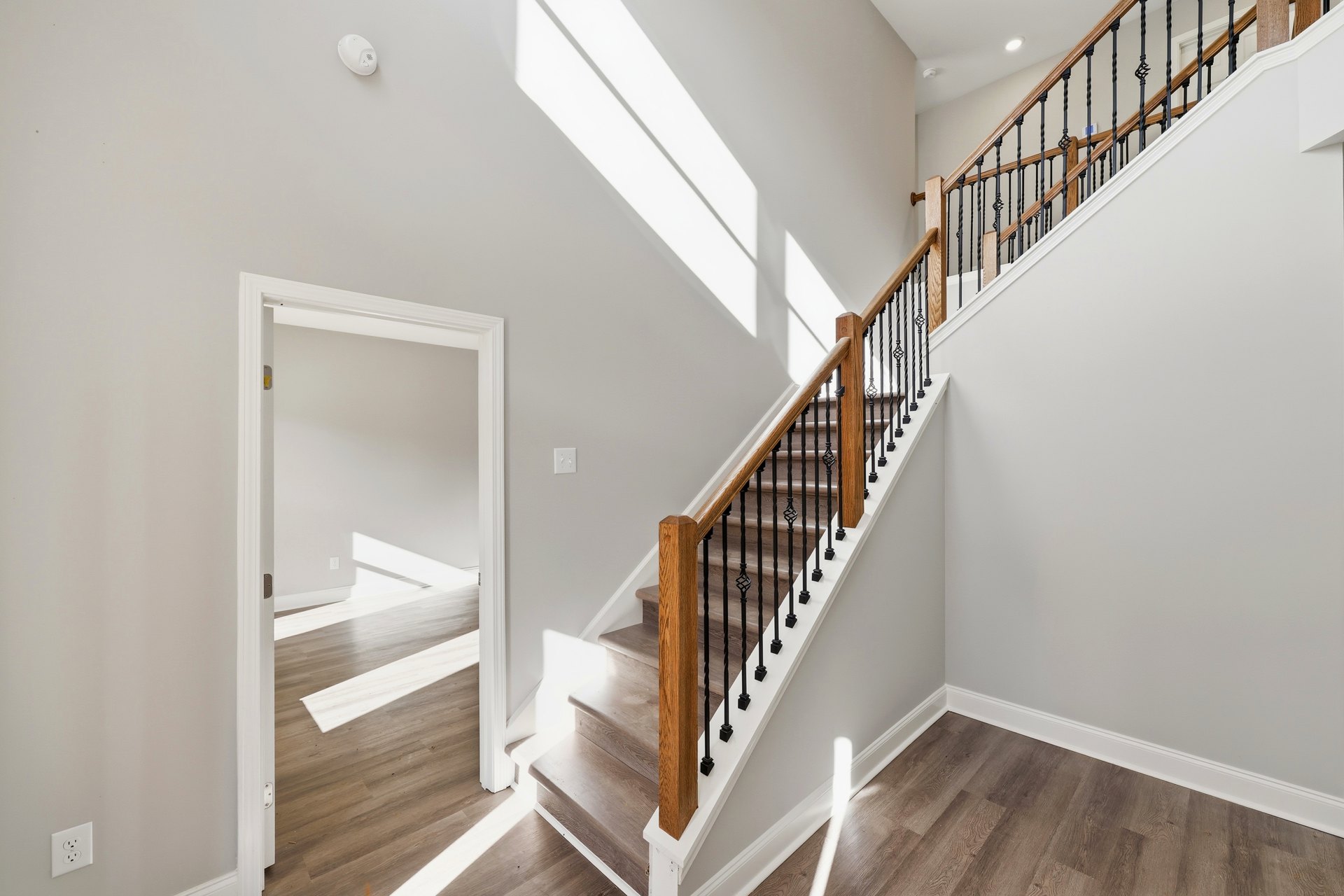Wood staircase with matching handrail and balusters, open door at landing, white plaster walls, hardwood flooring, and visible electrical outlet.
