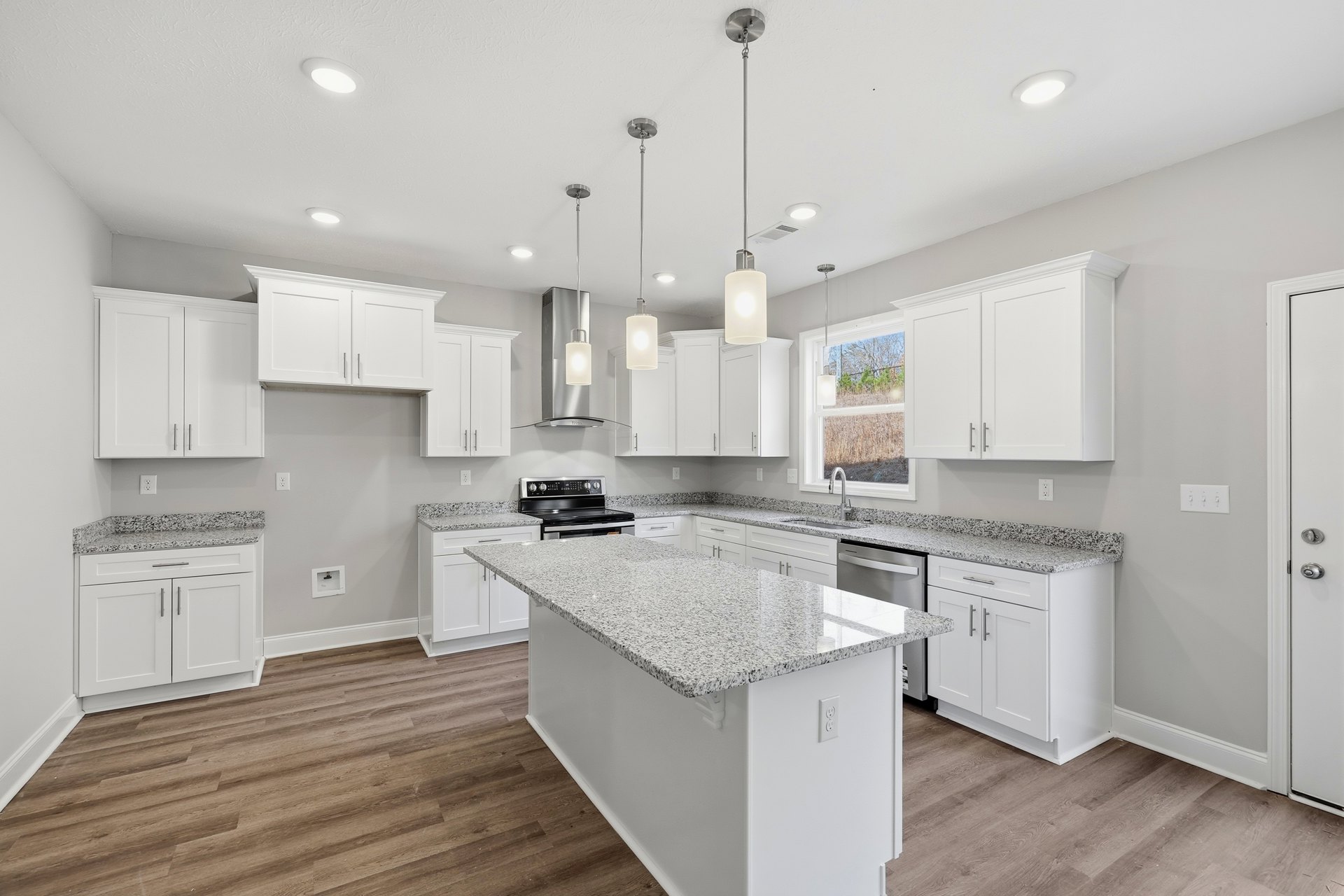 White kitchen with granite countertops, stainless steel stove, large granite island, brushed metal door handle, under-cabinet lighting, and white cabinetry.
