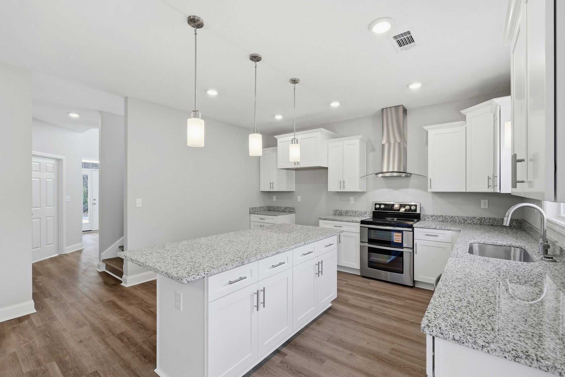 White kitchen with shaker cabinets, granite countertops, stainless steel stove, central island, undermount sink, and pendant lighting.