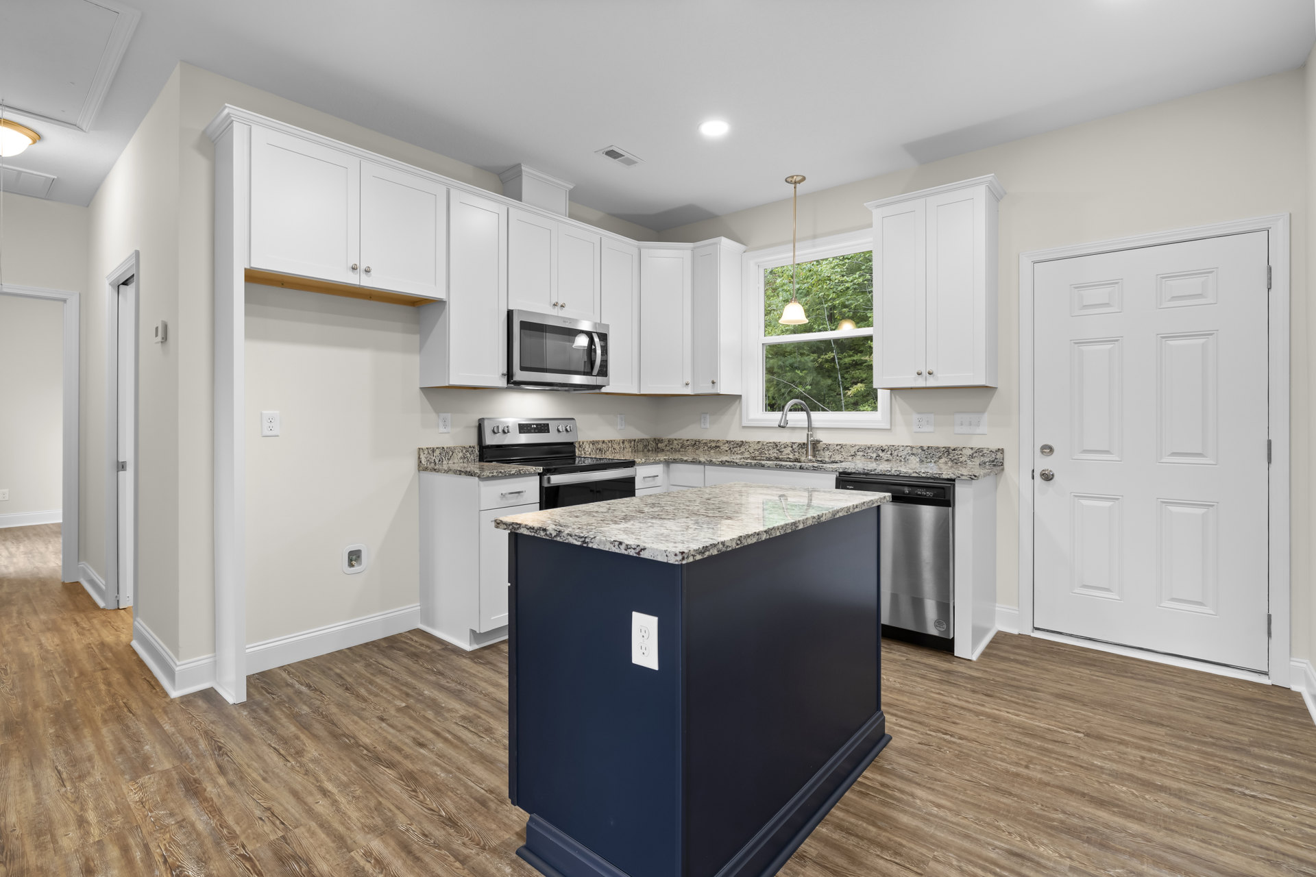 Marble kitchen island with waterfall edge, white shaker cabinets, stainless microwave, granite countertops, silver hardware, light wood flooring