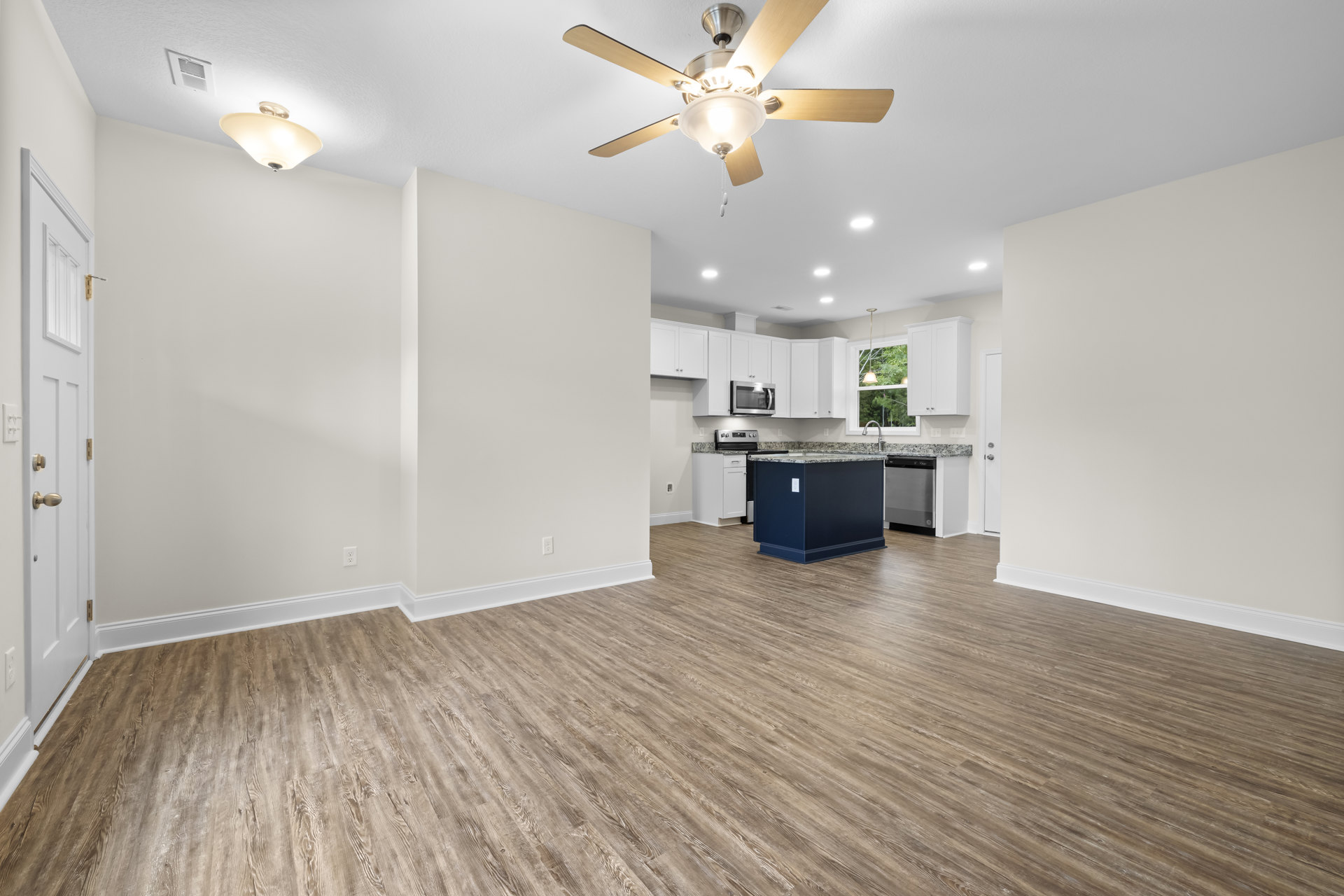 Open living area with wood flooring, blue baseboards, marble kitchen island, ceiling fan with light fixture, and neutral walls