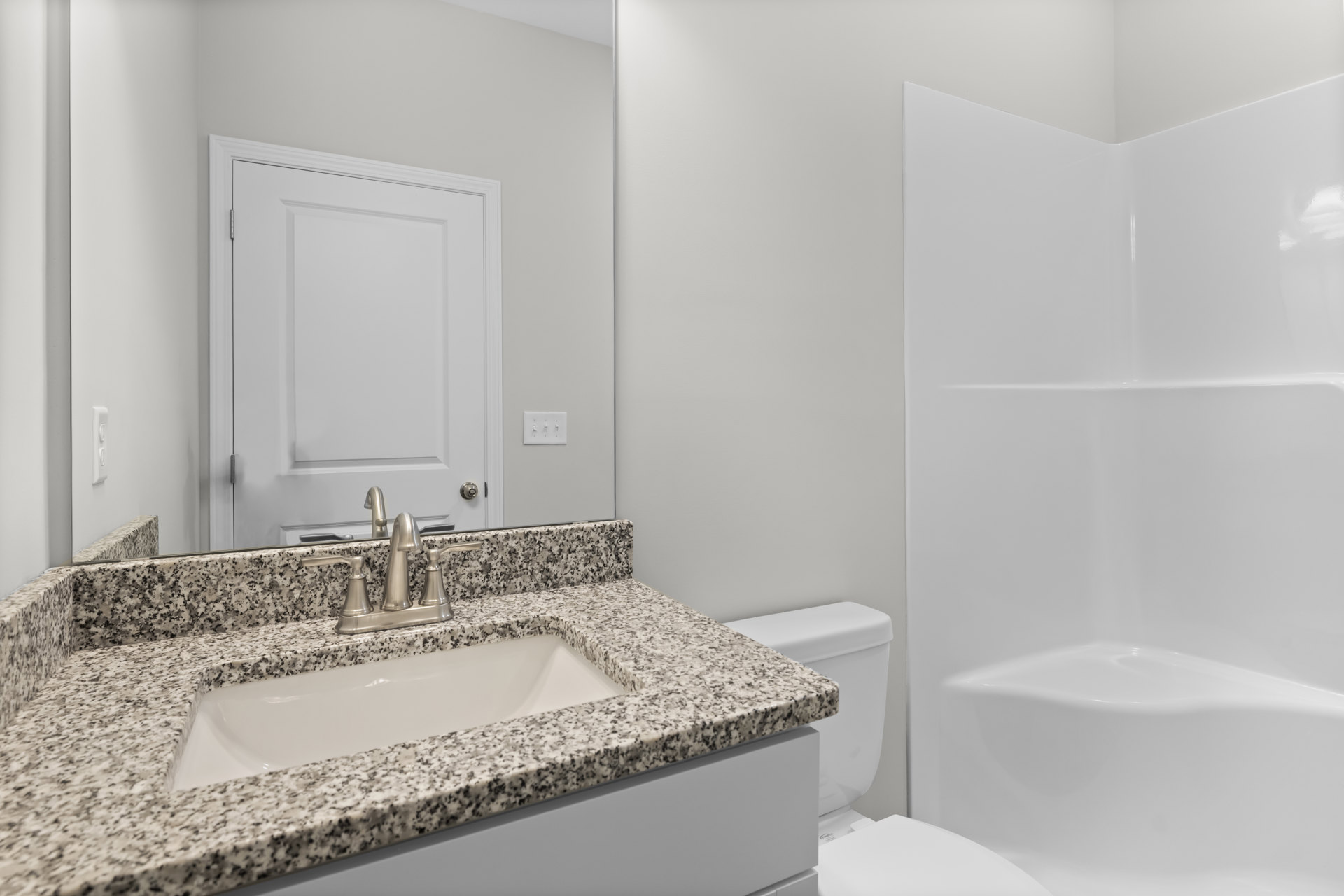 Modern bathroom with white ceramic sink and chrome faucet, adjacent toilet, light gray tile walls, white door with silver handle, and wall-mounted light switch