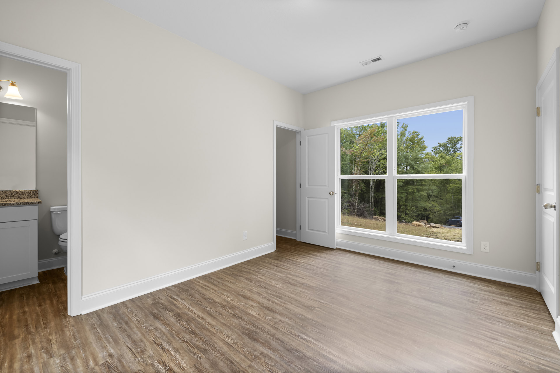Wood flooring in a bright room with white walls, a white door, and a large window framed in black, overlooking trees outside