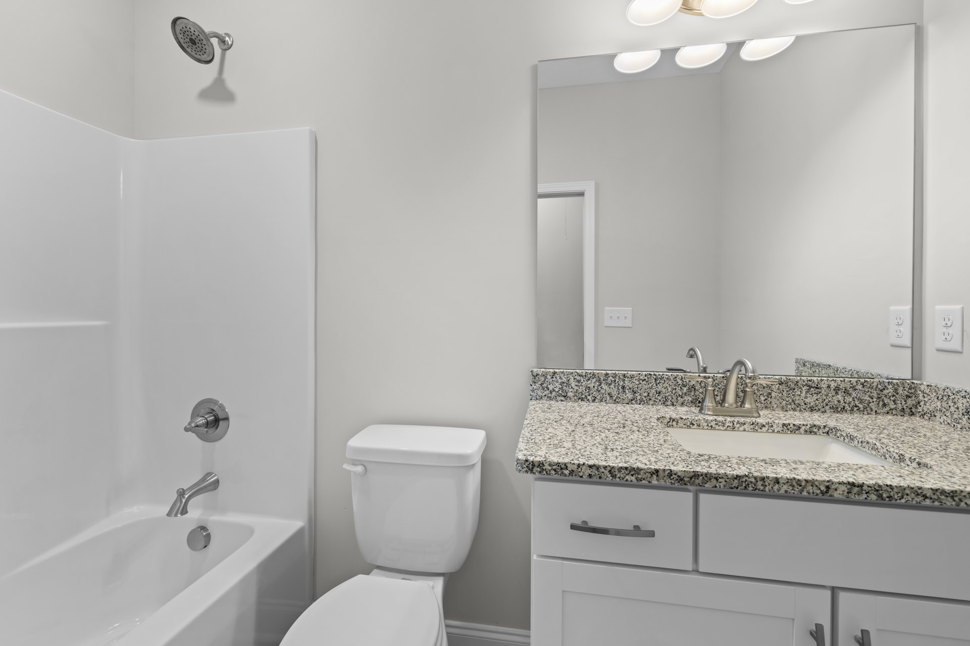 Modern bathroom with white porcelain sink and toilet, wall-mounted chrome faucet, tiled walls, built-in bathtub, and visible electrical outlet near the vanity