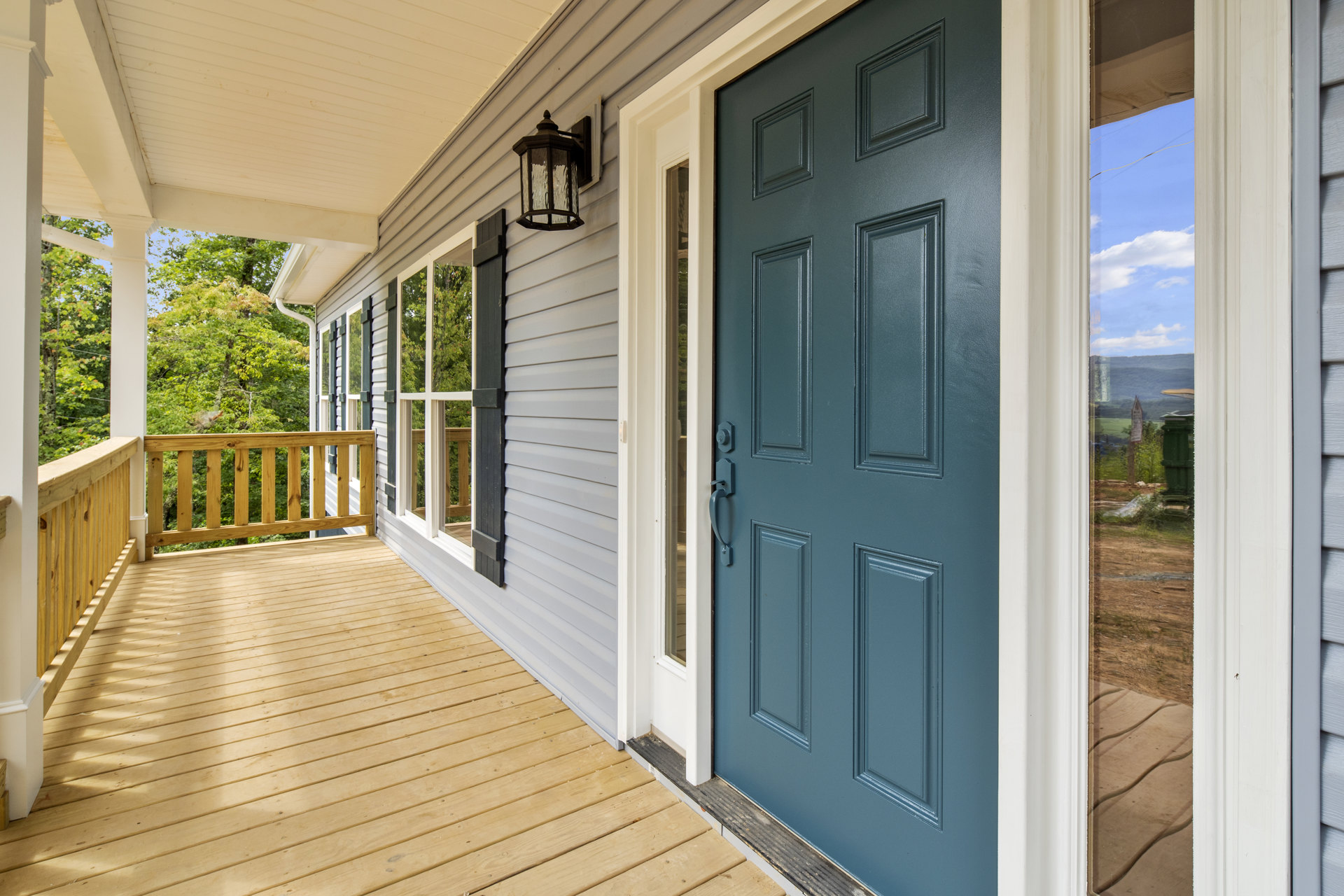 Blue front door with white trim, wooden porch railing, large windows, and surrounding trees