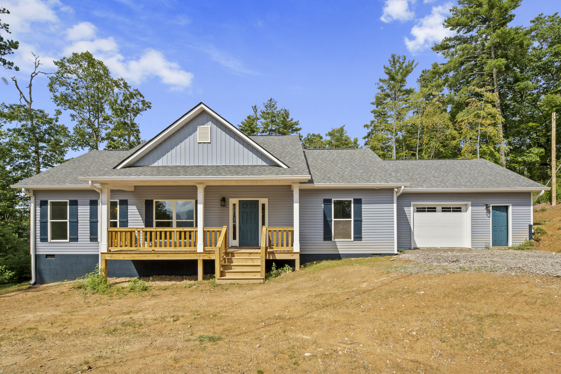 Two-story house with white siding, covered front porch, wooden deck with railing, blue front door with glass panels and white trim, attached garage, large windows, wooden stairs