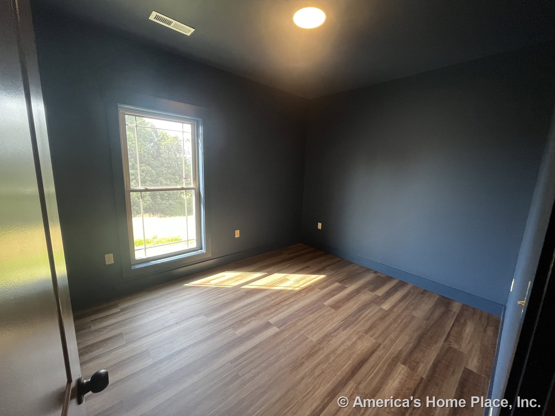 Bedroom with dark blue painted walls, single large window, wood-look vinyl plank flooring, recessed ceiling light, white baseboard trim, and ceiling vent.