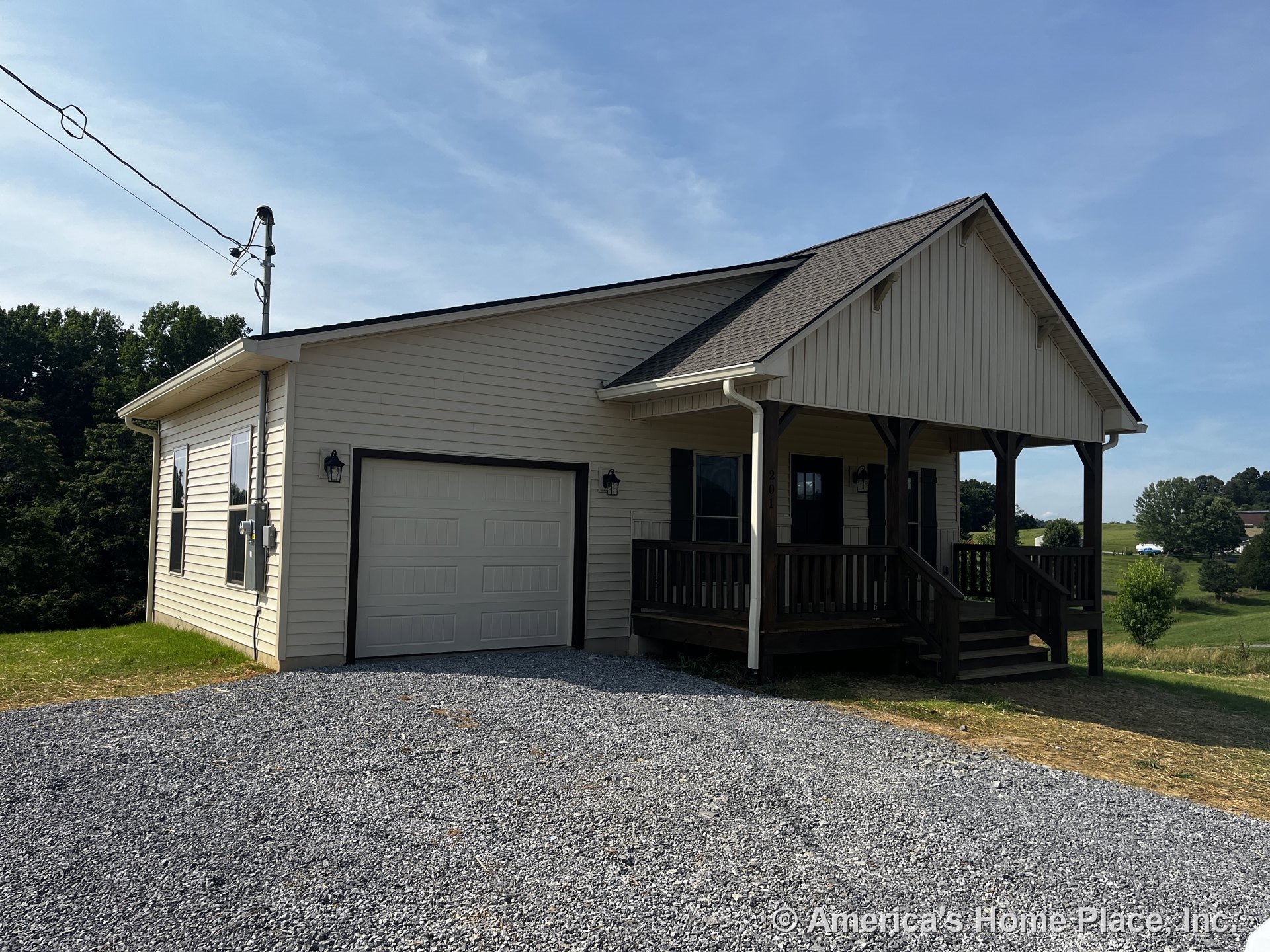 Covered front porch with wood railings, single-car garage door, vinyl siding exterior, asphalt shingle roof, gravel driveway, exterior lighting, white trim, front steps, and