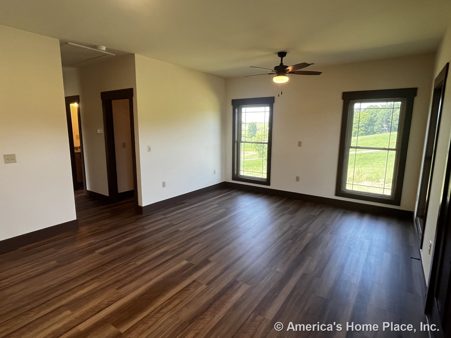Living room with two tall windows framed in dark trim, wood-look plank flooring, ceiling fan with integrated light, neutral walls, dark baseboards and door trim, open doorway