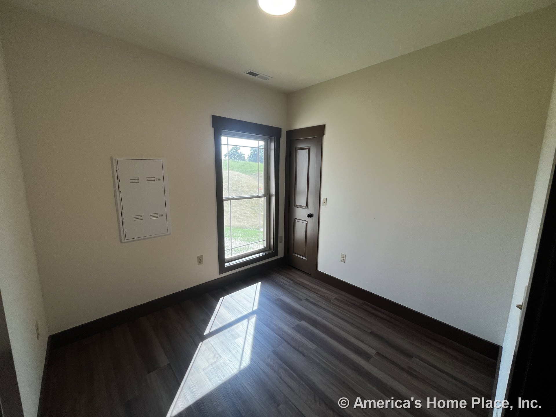 Small room with dark wood baseboards and trim, large window framed in wood, vinyl plank flooring, flush ceiling light, utility access panel, wood interior door, neutral walls, and