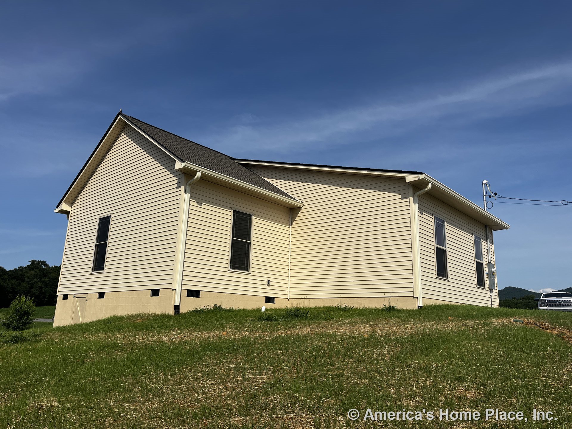 Beige vinyl siding exterior with dark shingled gable roof, double-hung windows framed by white trim and gutters, raised foundation, and utility meter mounted on side wall.