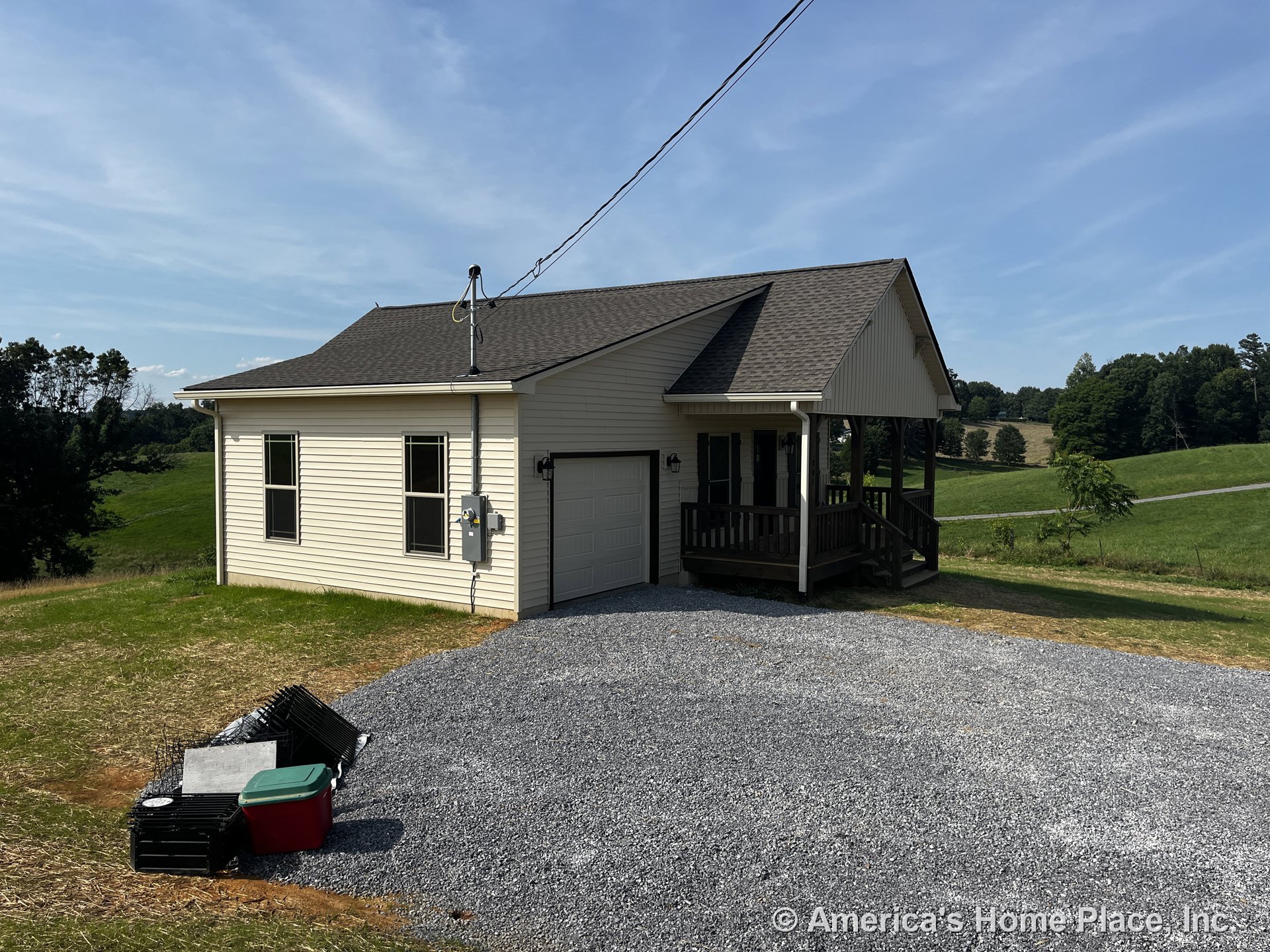 Covered front porch with wood railing, attached single-car garage, vinyl siding exterior, asphalt shingle roof, double-hung windows, gravel driveway, and contrasting exterior trim