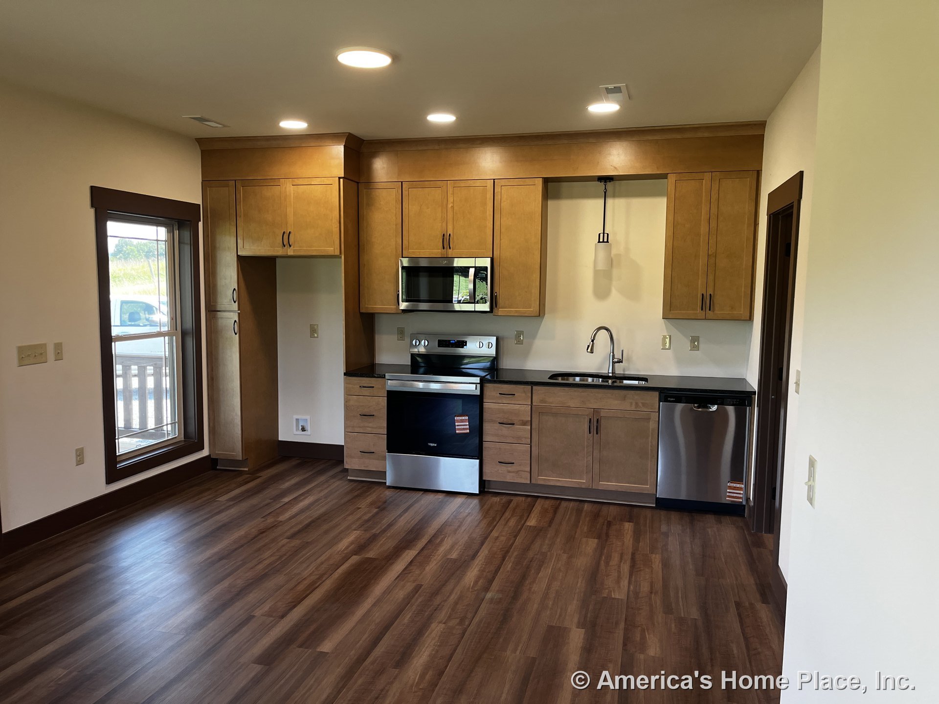 Wood cabinetry with upper and lower storage, stainless steel oven, built-in microwave, and dishwasher, single basin sink with gooseneck faucet beneath a large window with wood