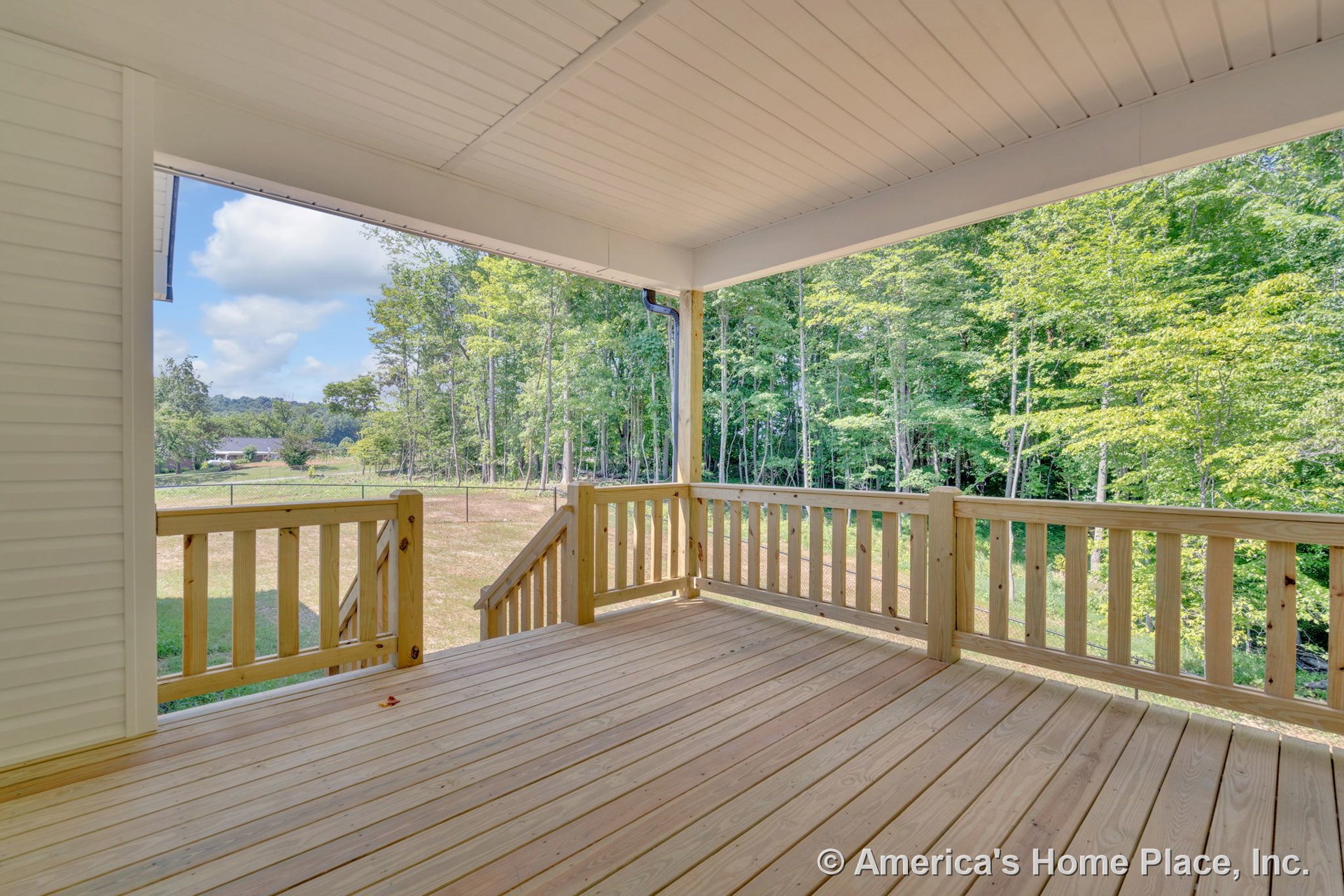 Covered porch with natural wood deck flooring and railings, white paneled ceiling, outdoor stairs leading to backyard, and open view framed by permanent trim.