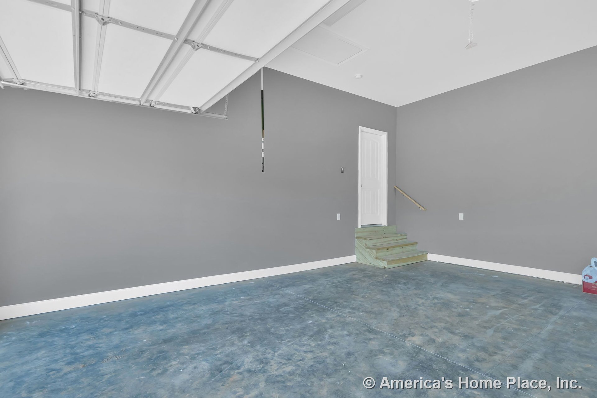 Concrete garage floor, gray painted walls, white overhead garage door, wooden steps with handrail leading to interior access door, white baseboard trim, unfinished stairs, ceiling