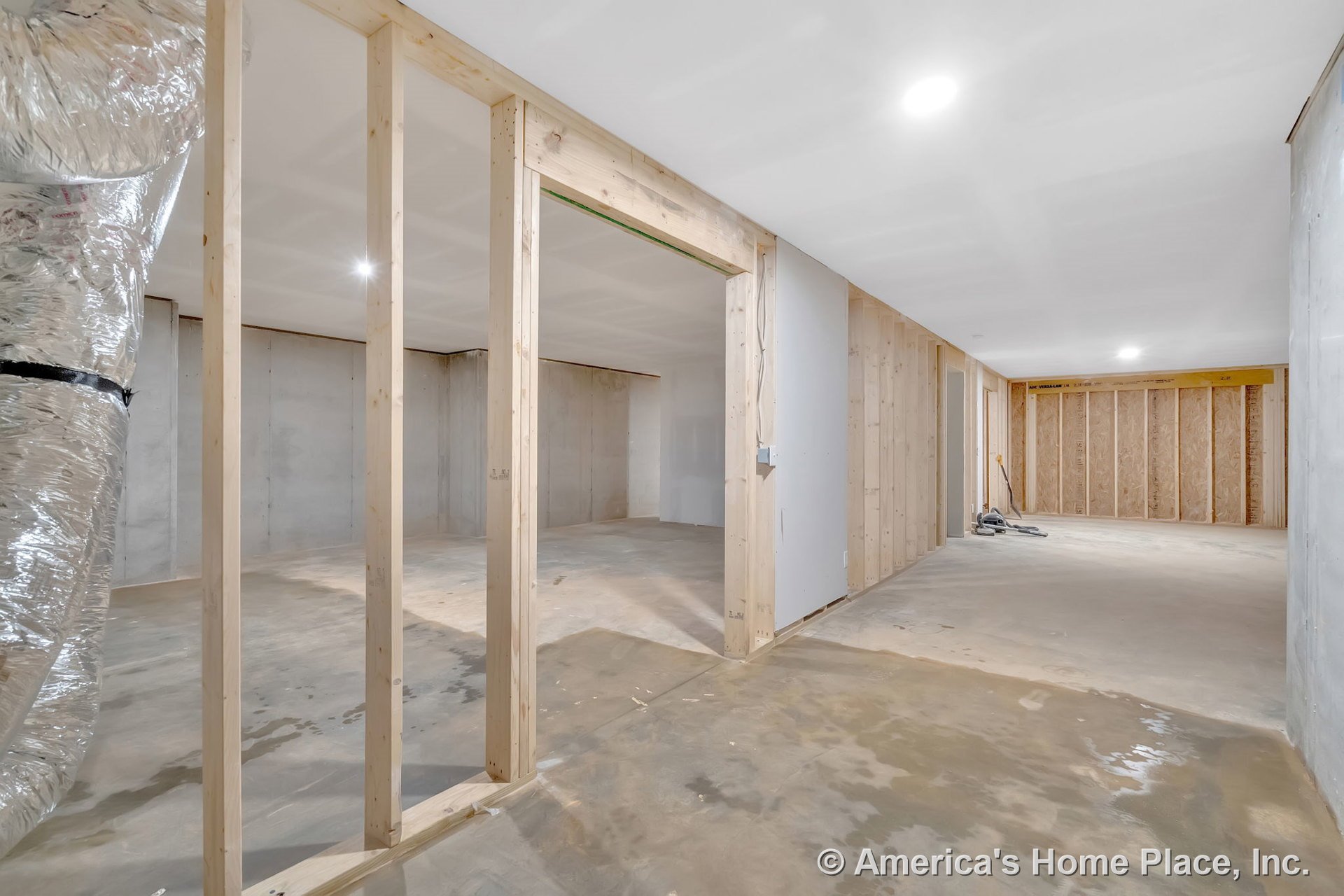 Unfinished basement with exposed wood framing, concrete slab flooring, unfinished drywall, recessed ceiling lights, visible utility ductwork, and open wall studs.