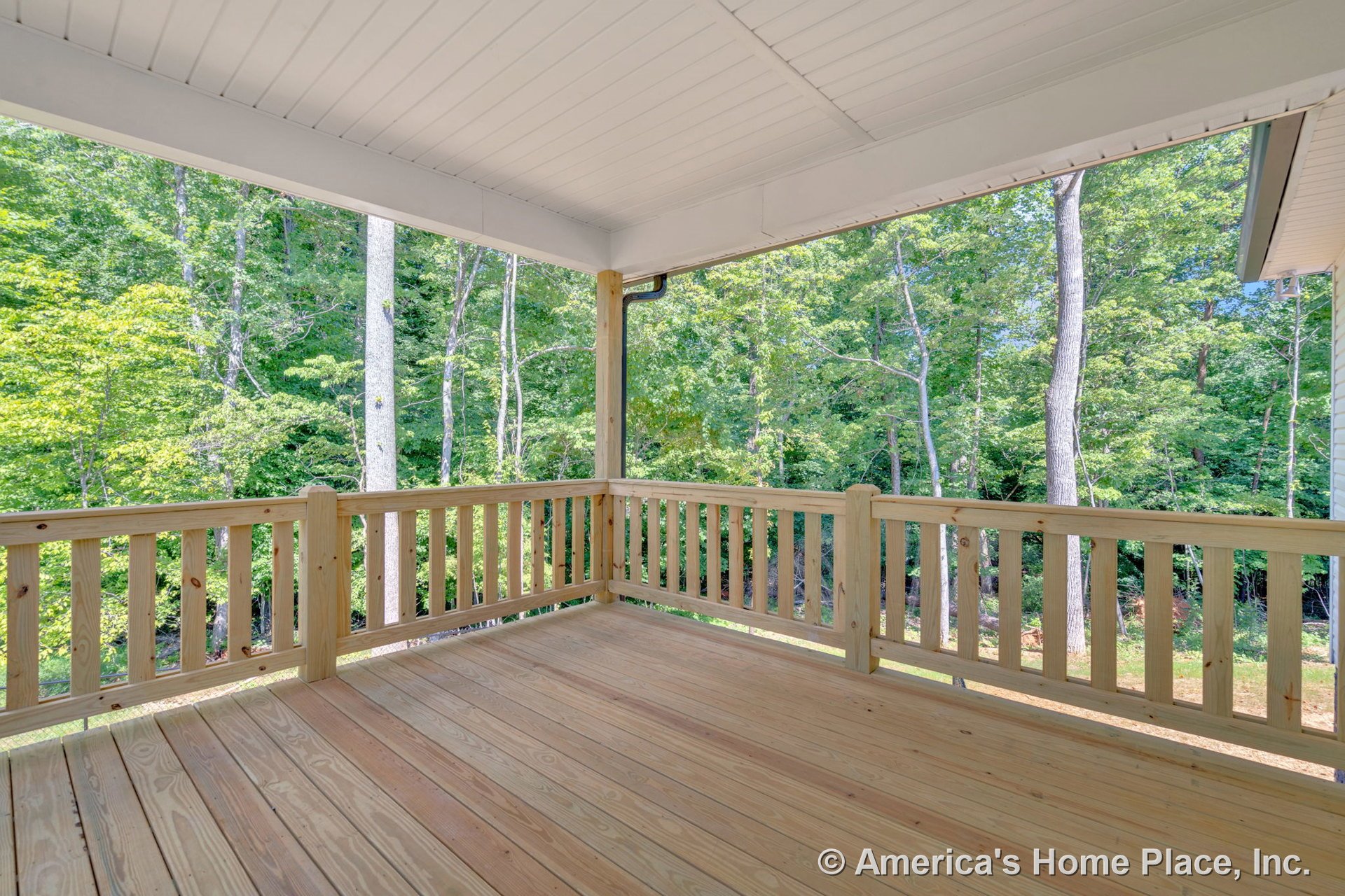 Covered porch with natural wood plank flooring and matching wooden railings, detailed trim, and a covered ceiling, overlooking a wooded landscape through an open view.