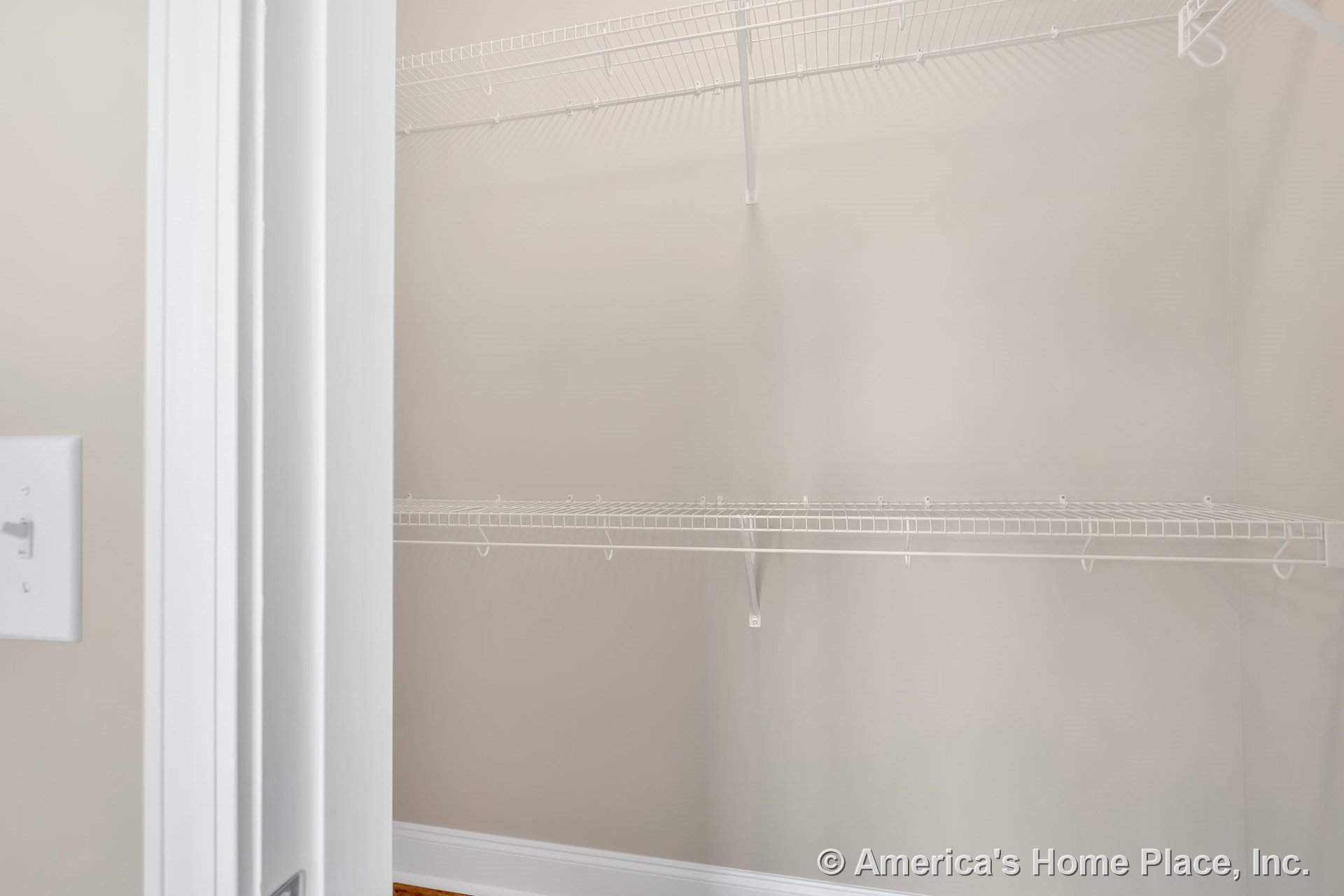 Walk-in closet with built-in white wire shelving, neutral painted walls, baseboard trim, closet door frame, and wall switch plate.