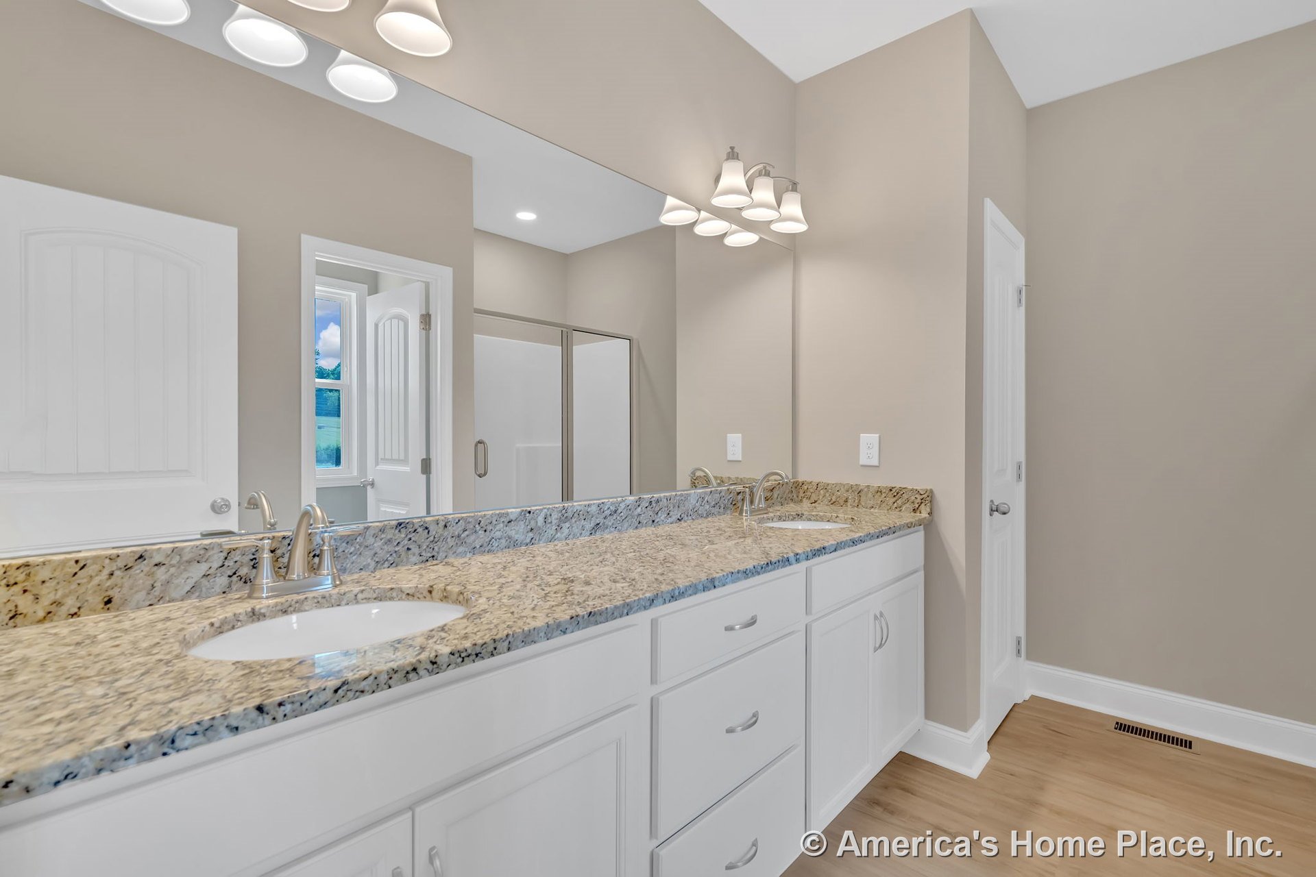 Double vanity with granite countertop, white cabinetry, undermount sinks, chrome faucets, large wall mirror, built-in vanity lighting, wood-look flooring, neutral wall color, and