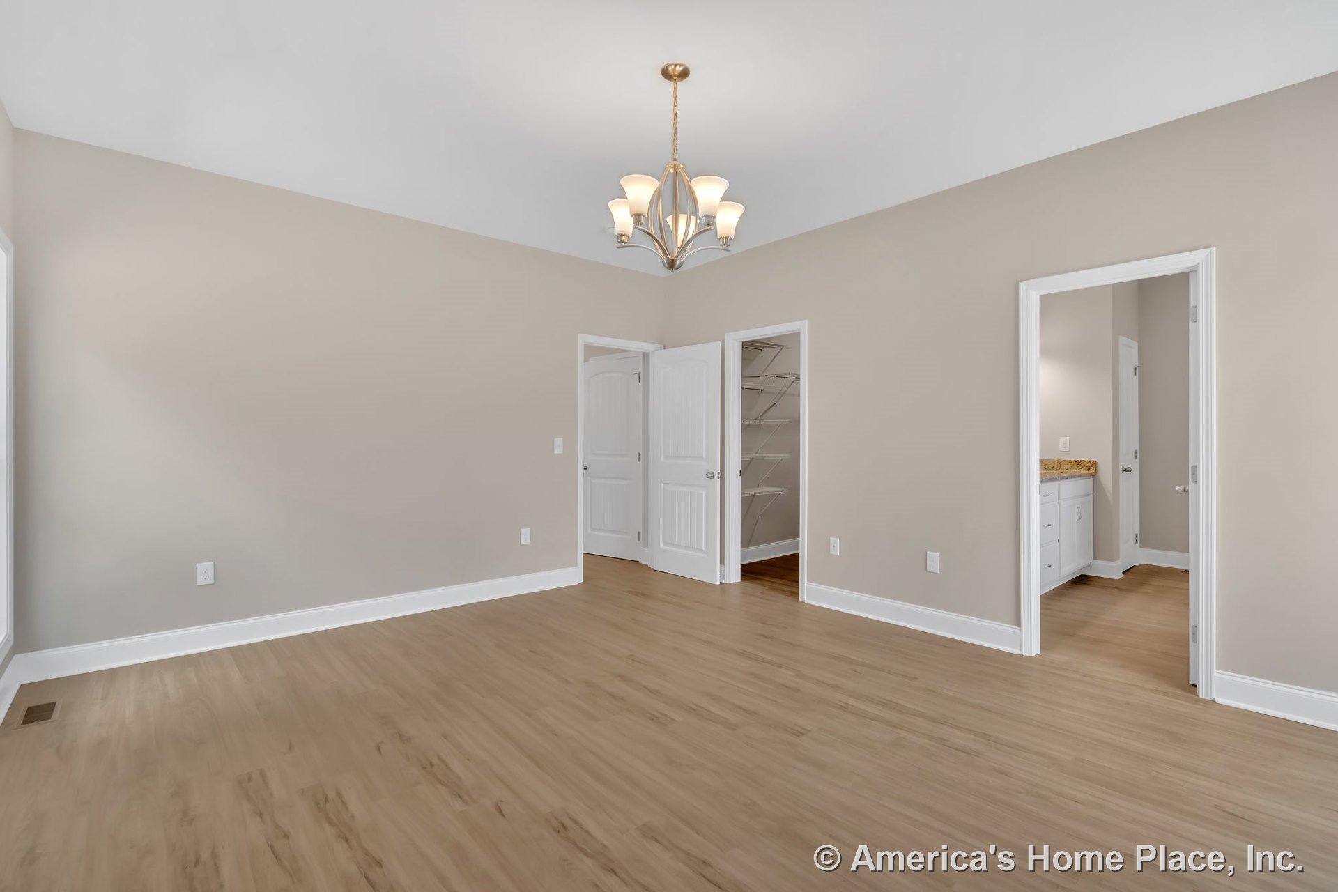 Bedroom with light wood flooring, beige walls, white baseboards and trim, central chandelier, double panel doors, walk-in closet with wire shelving, and entry to bathroom featuring