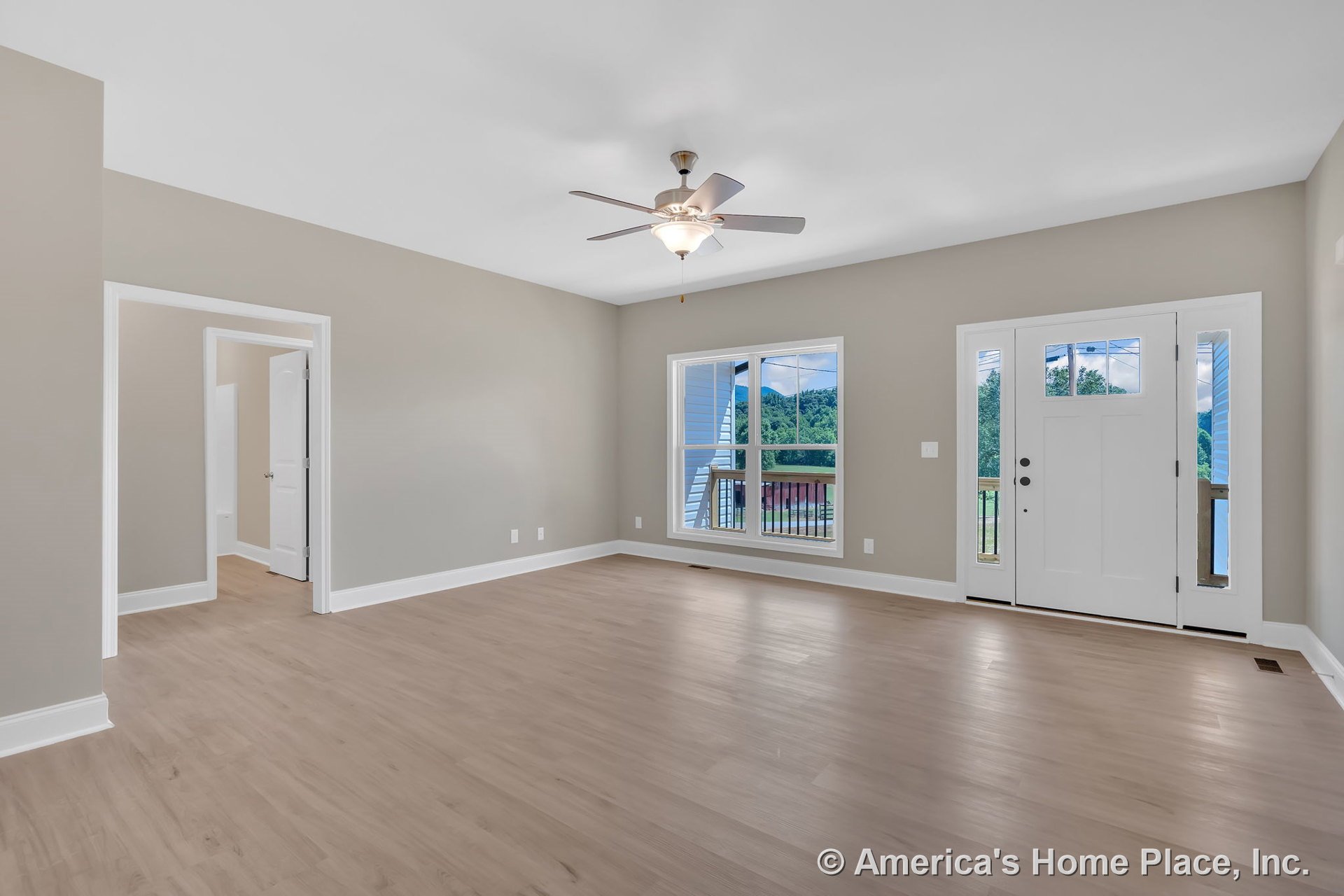 Light wood flooring, ceiling fan with integrated lighting, large double windows, white front door with glass panels, neutral walls, white baseboards and trim.