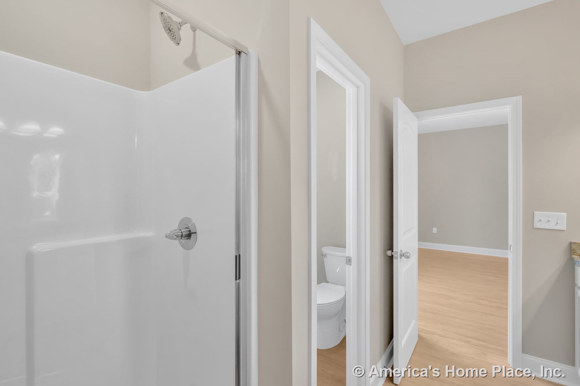 Walk-in shower with white surround and glass door, bathroom with toilet, light wood flooring extending into adjacent room, white trim and doors, neutral wall paint, baseboard, and