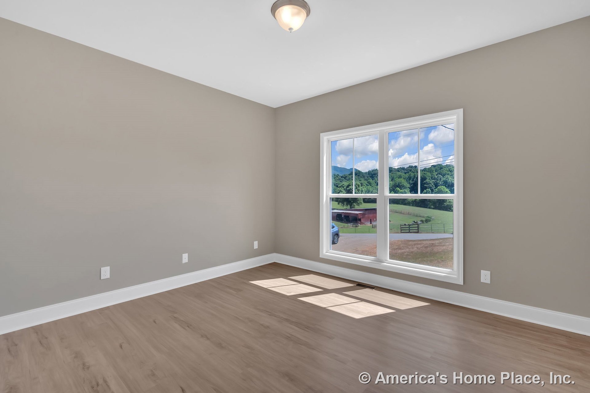 Bedroom with light wood flooring, beige painted walls, large double window framed in white trim, white baseboards, and a flush mount ceiling light.
