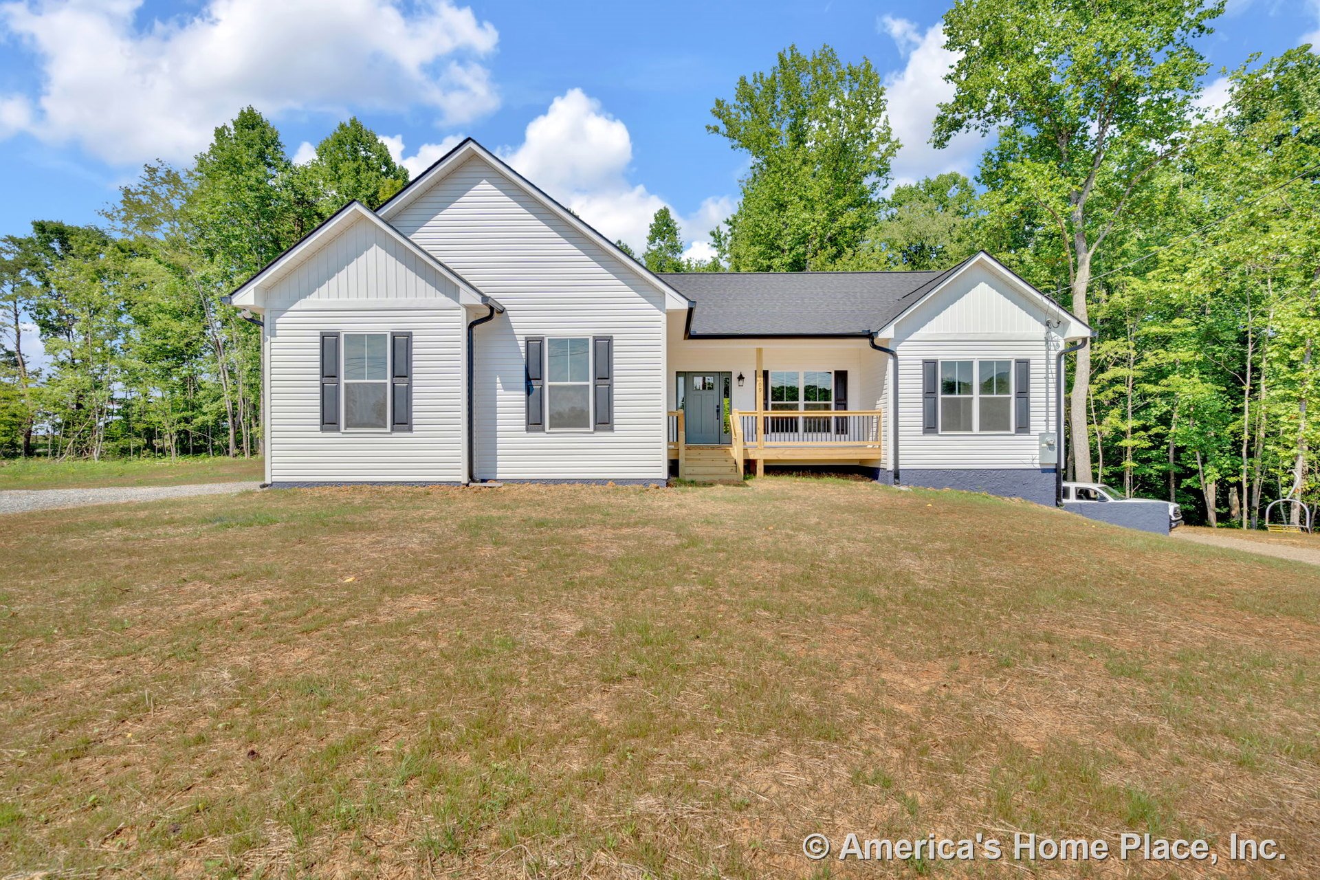 White vinyl siding exterior with black window shutters, gabled roof, covered front porch featuring wood railings, multiple double-hung windows, permanent lighting, entry door, and
