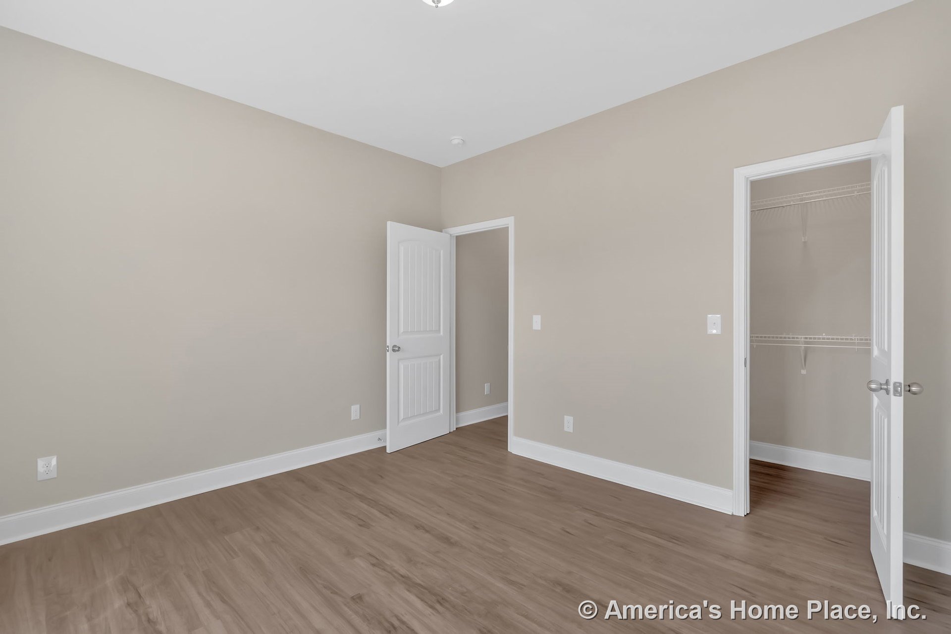Bedroom with light wood plank flooring, beige walls, white baseboard trim, paneled white doors, flush ceiling light fixture, and walk-in closet featuring wire shelving.