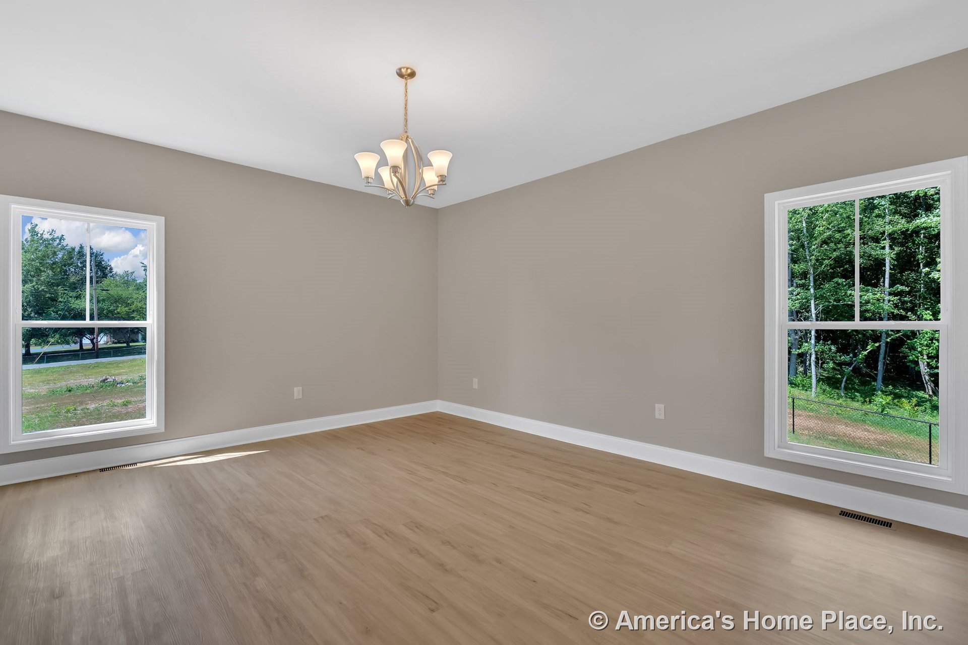 Spacious living room with light wood flooring, two large double-hung windows, modern ceiling chandelier, neutral wall color, white baseboard trim, and flat ceiling.