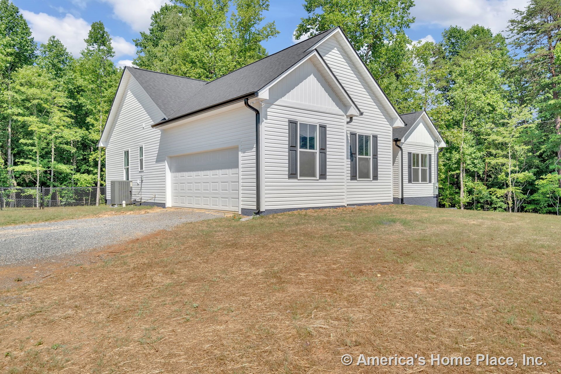White vinyl siding exterior with gable roof, attached two-car garage, double-hung windows framed by shutters, gravel driveway, and black gutter system along roofline.