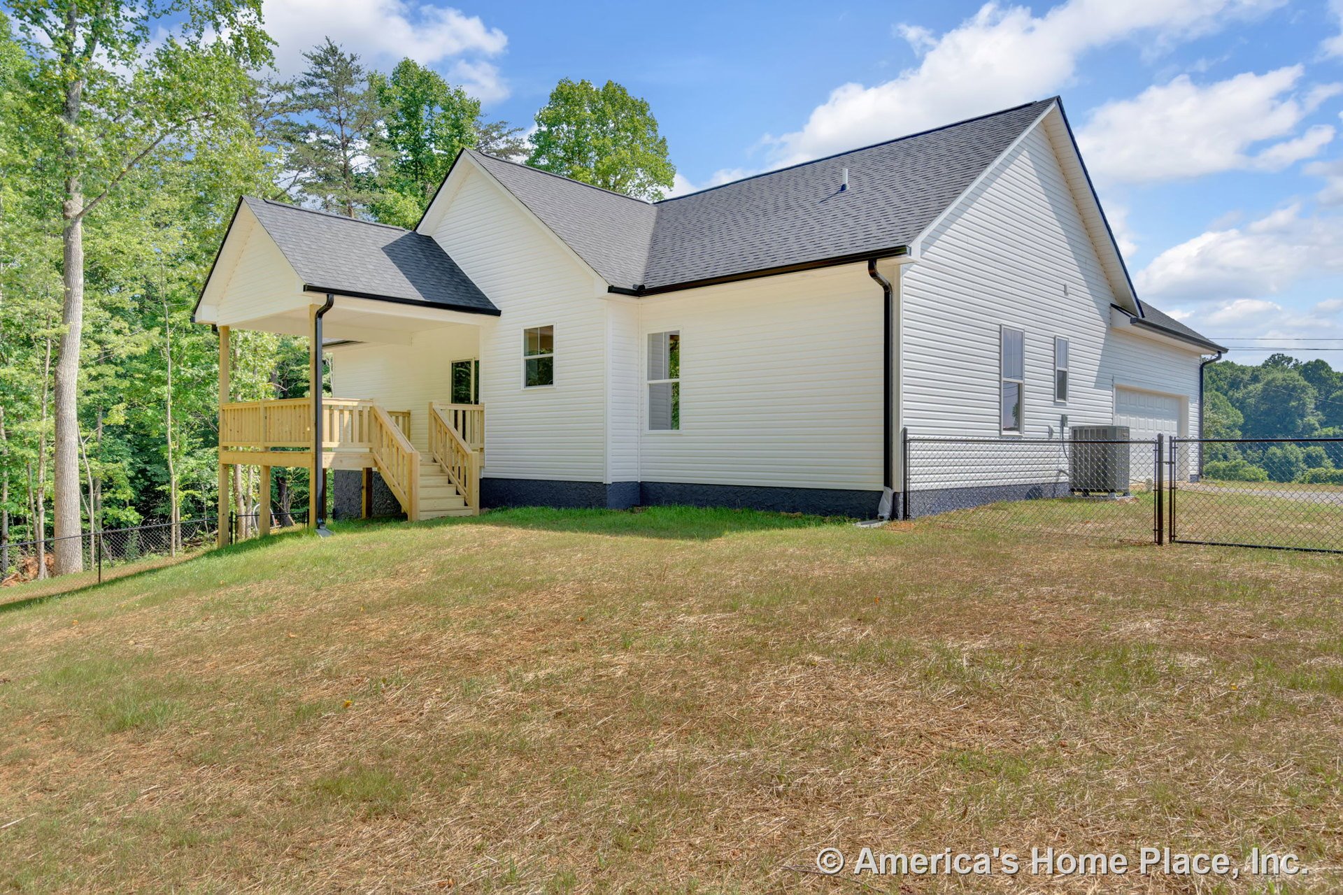 White vinyl siding exterior with black shingle roof, multiple rectangular windows, attached two-car garage, covered back porch featuring wood railing and stairs, fenced backyard