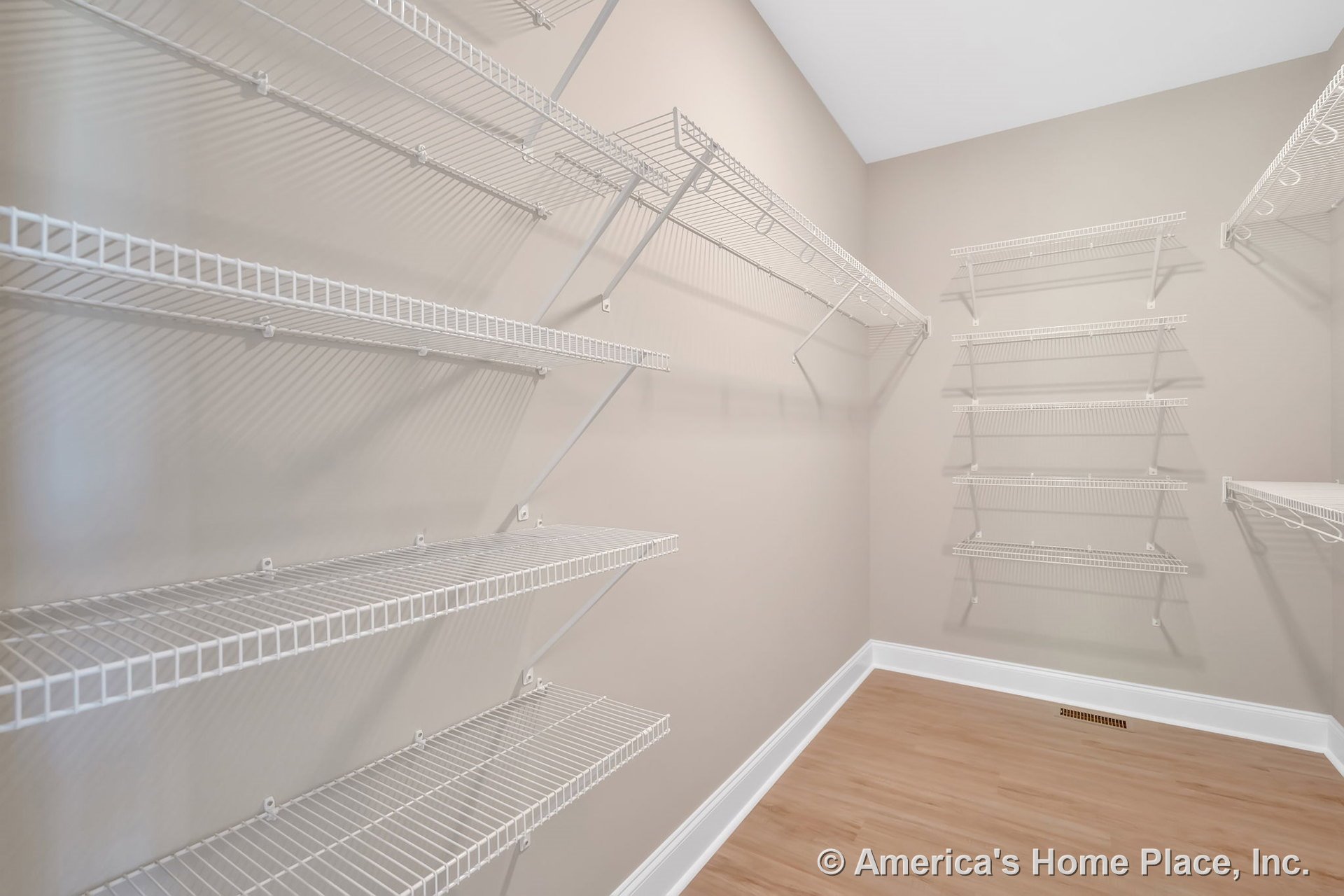 Walk-in closet with multiple white wire shelving units, light wood flooring, beige painted walls, white baseboard trim, and floor vent.