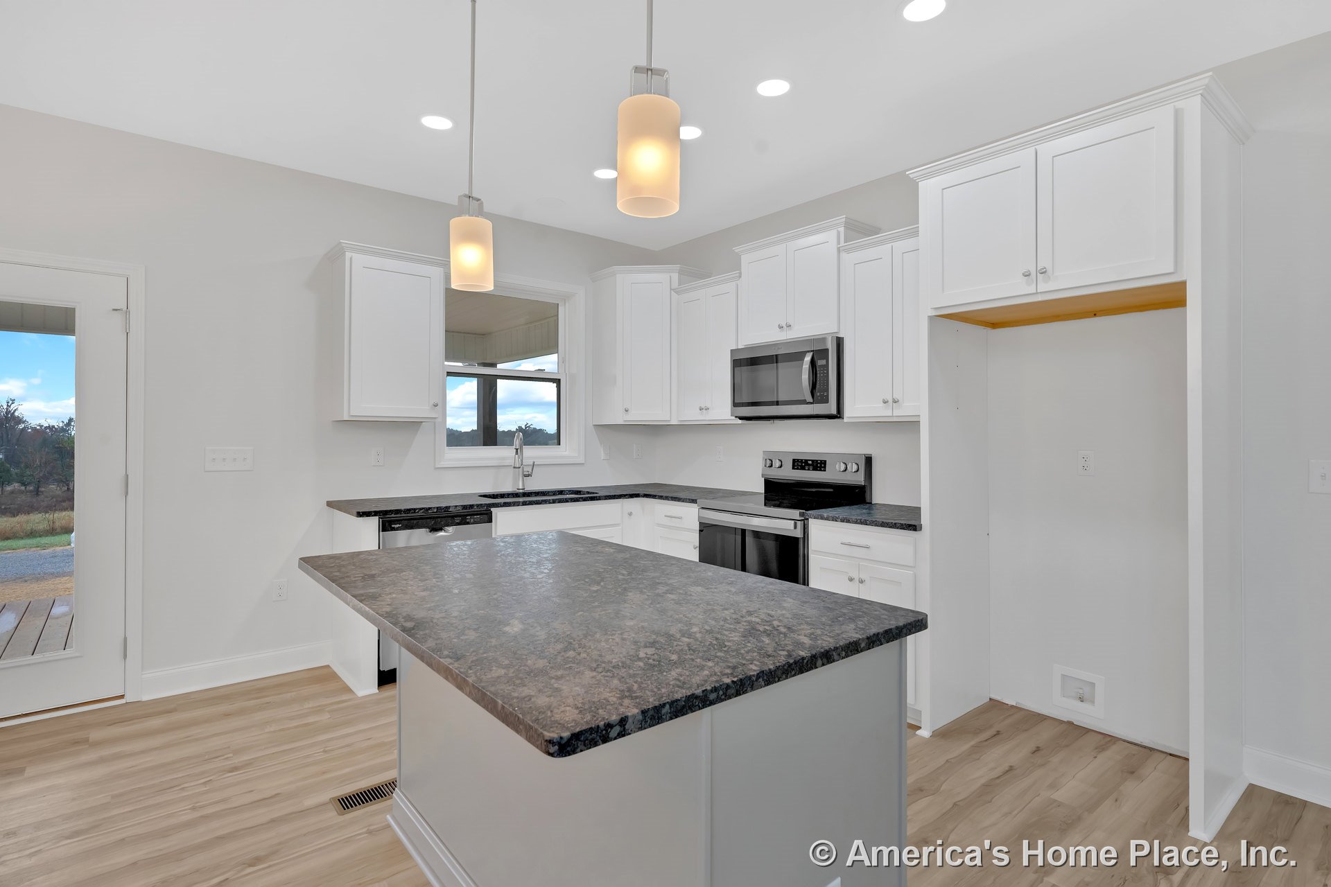 Kitchen with center island featuring dark countertop, white upper and lower cabinetry, stainless steel microwave and oven, pendant and recessed ceiling lights, window above sink