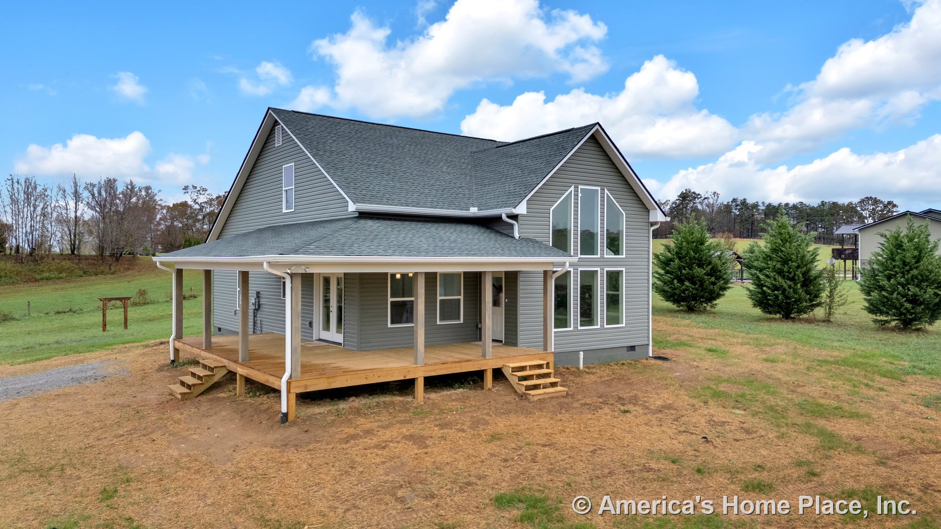Large covered wraparound porch with wooden steps, prominent floor-to-ceiling windows on the front facade, gray vinyl siding, gable roof with asphalt shingles, white trim and