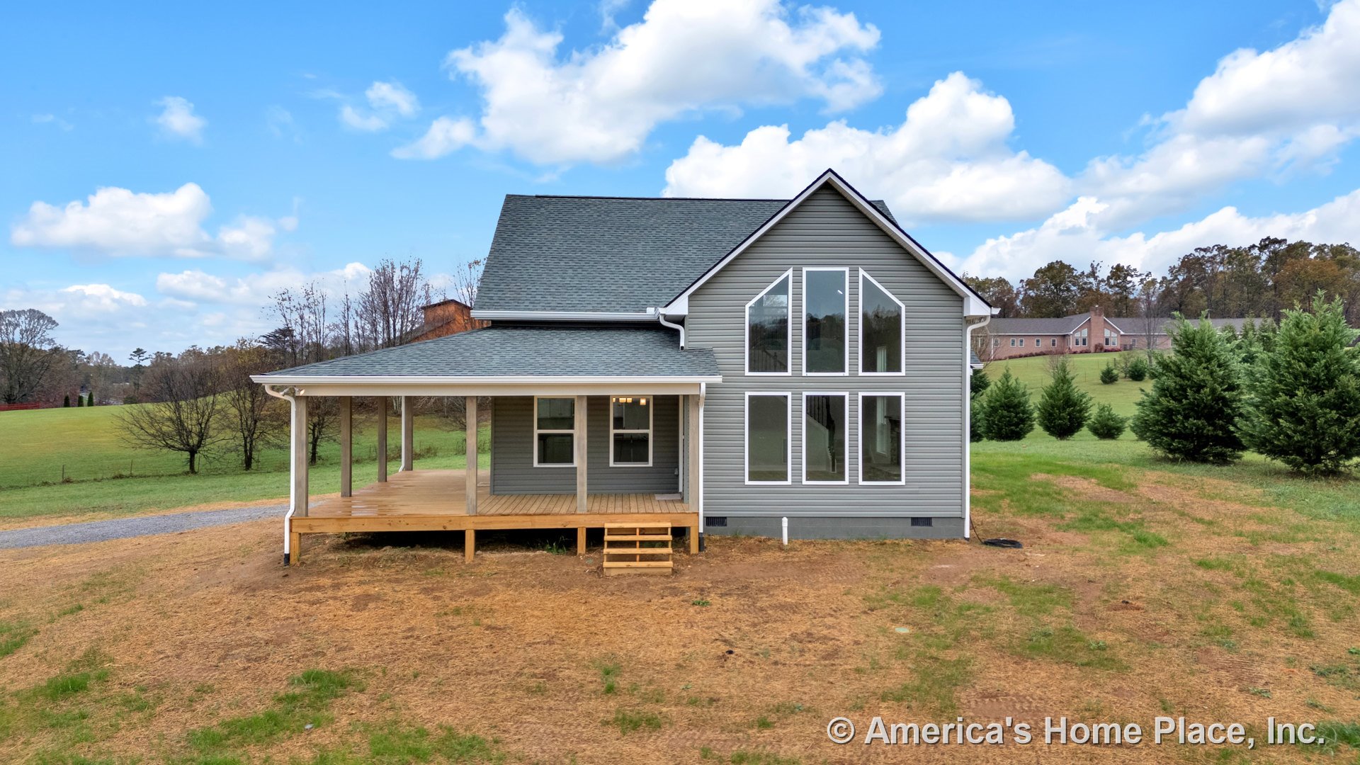 Large covered front porch with wood decking, multiple floor-to-ceiling windows, gray vinyl siding exterior, gable roof with asphalt shingles, white trim around windows and doors
