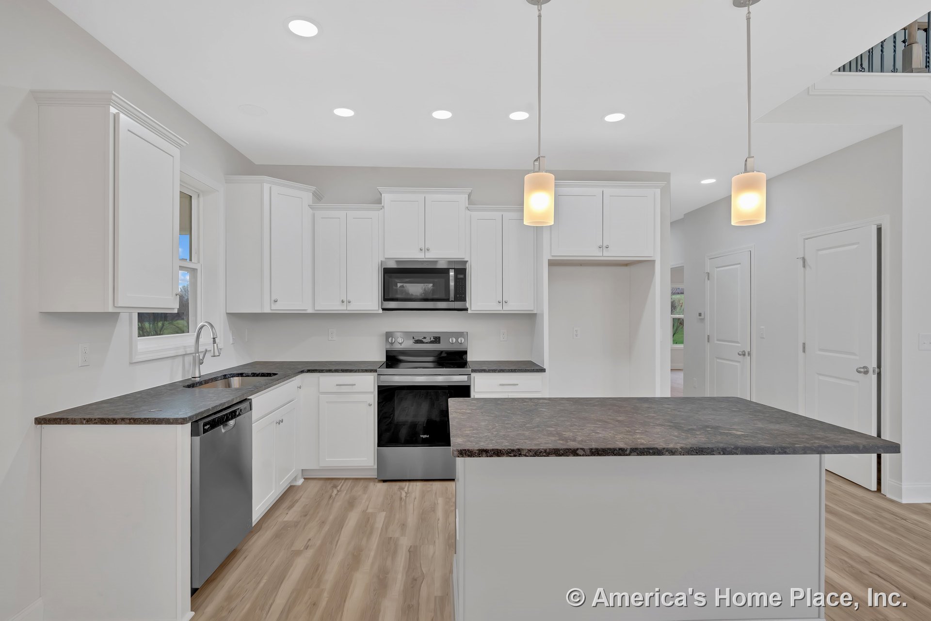 White shaker cabinets with dark laminate countertops, stainless steel oven and microwave, pendant and recessed ceiling lights, wood-look vinyl flooring, kitchen island with
