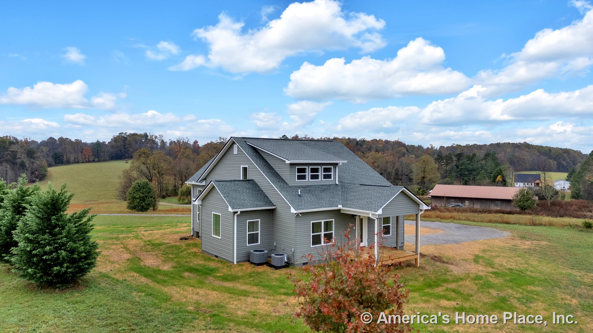 Gray vinyl siding exterior with white trim, gabled asphalt shingle roof, covered front porch, multiple double-hung windows, exterior HVAC units, landscaped front entry in rural