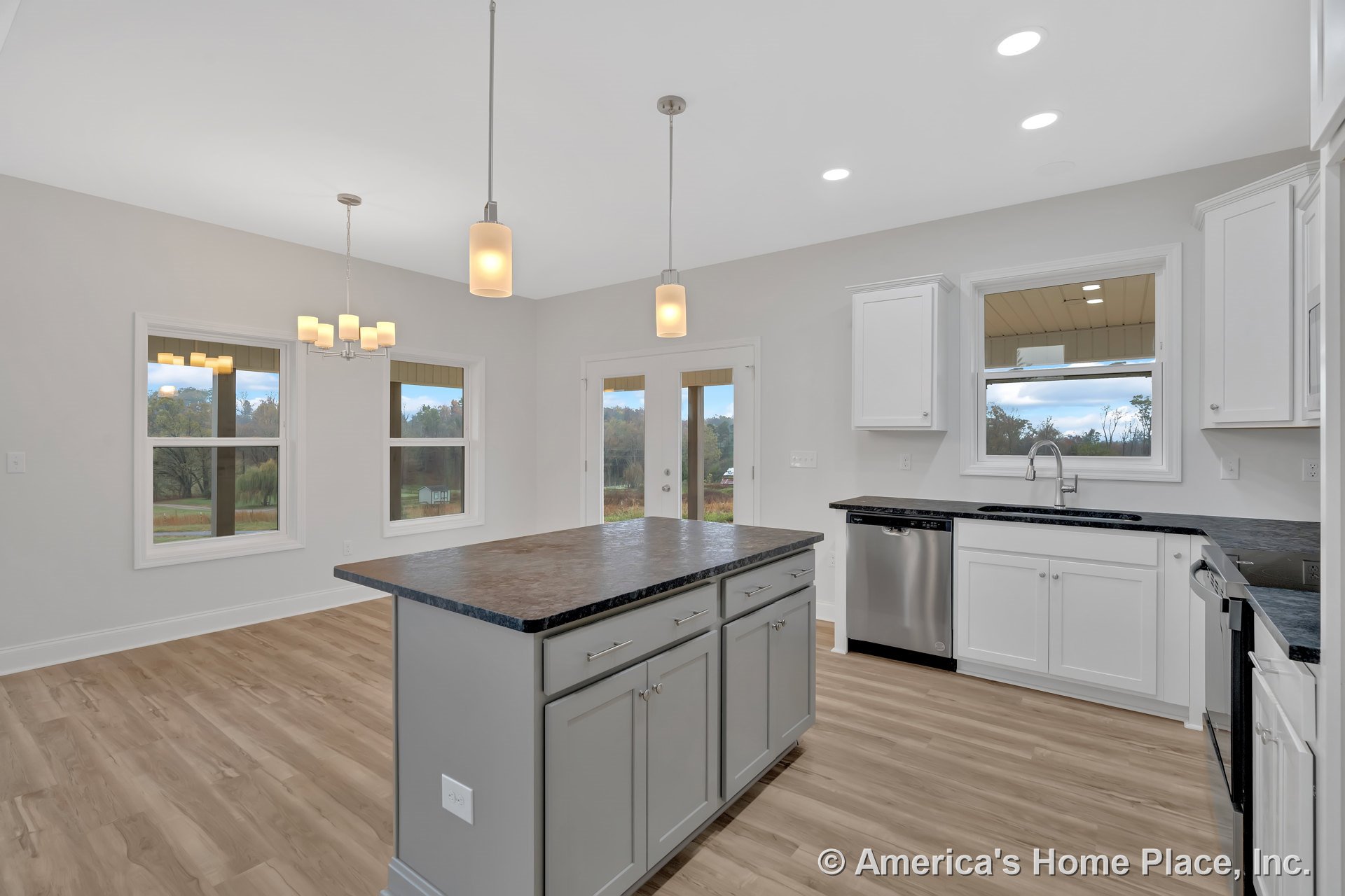 Custom kitchen with white upper and lower cabinets, dark stone countertops, stainless steel appliances, storage island, pendant and recessed lighting, light wood flooring, double